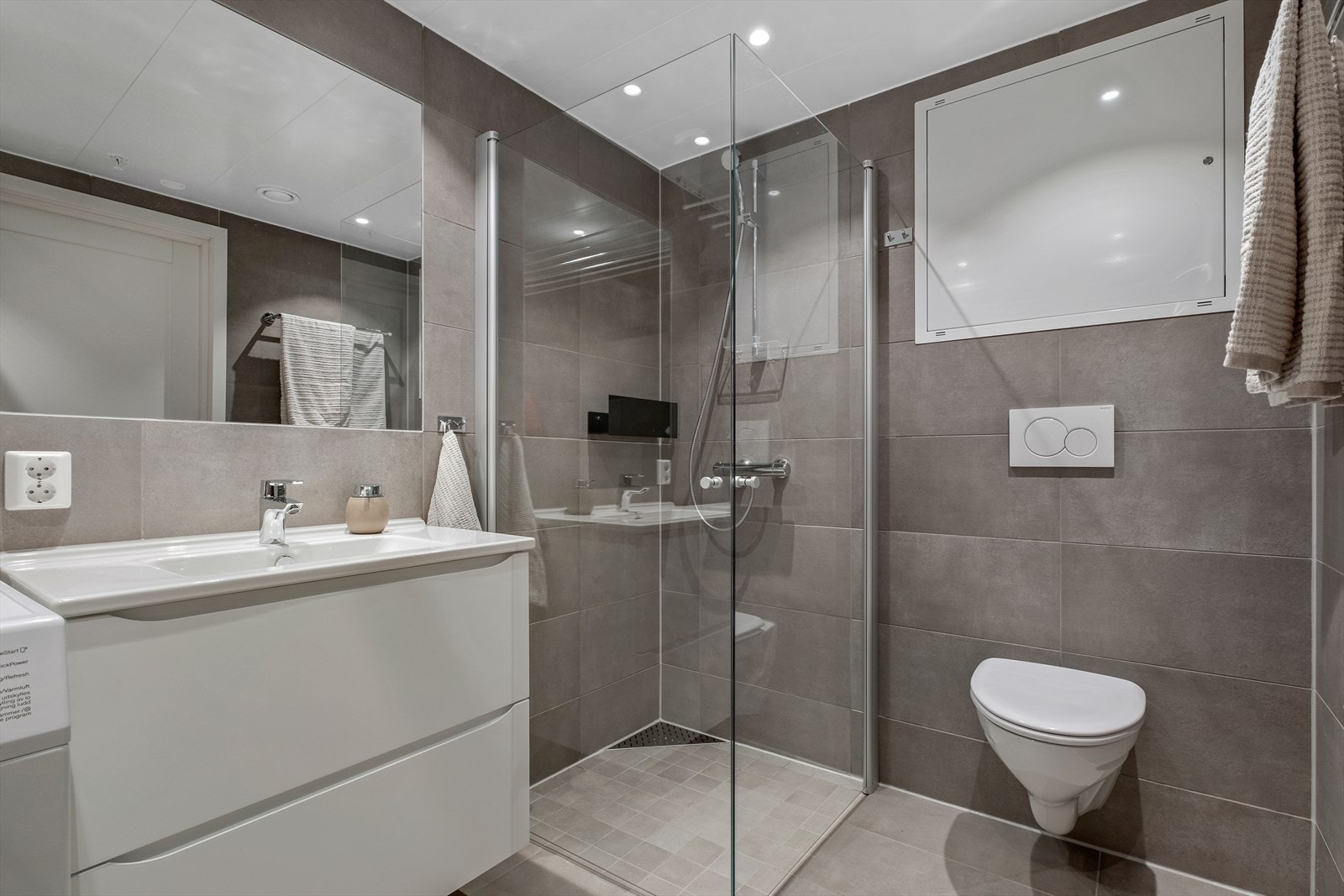 Rommet er videre utstyrt med innfellbare dusjdører, mekanisk avtrekk, opplegg for vaskemaskin, rørfordelingsskap, servantskap, stoppekran, vannmåler og veggmontert wc. Galleribilde