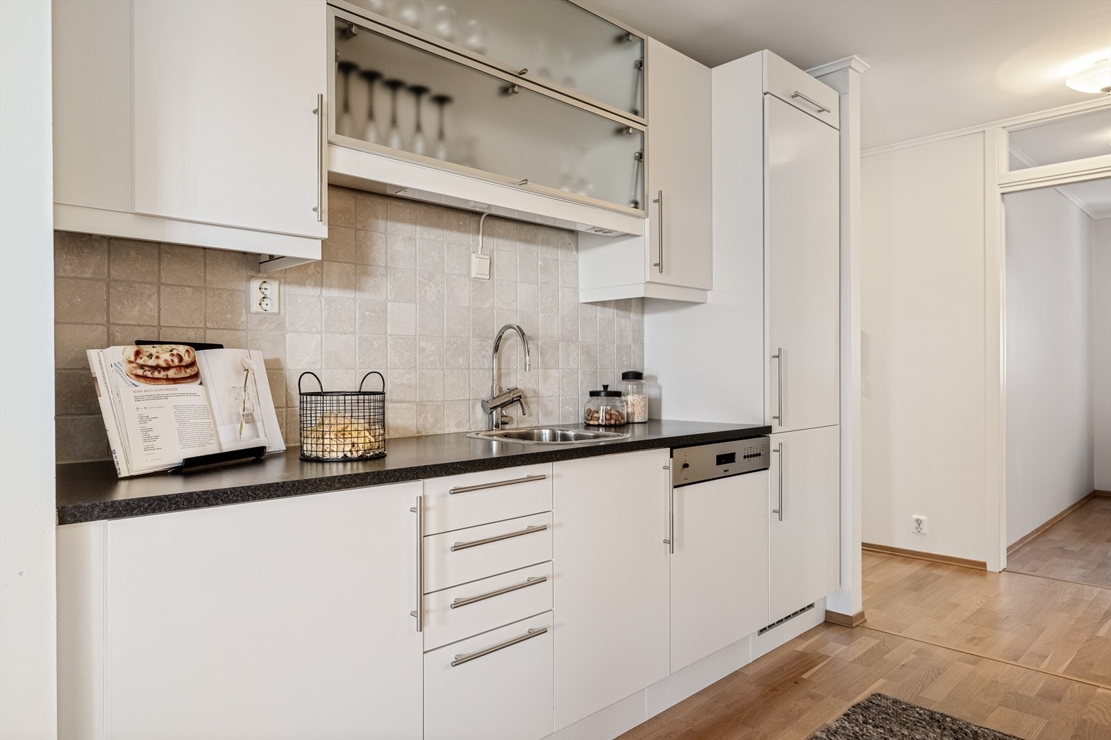 Lyst kjøkken med integrerte hvitevarer som blant annet frys- og kjøleskap, oppvaskmaskin, stekeovn, platetopp og ventilator. Galleribilde