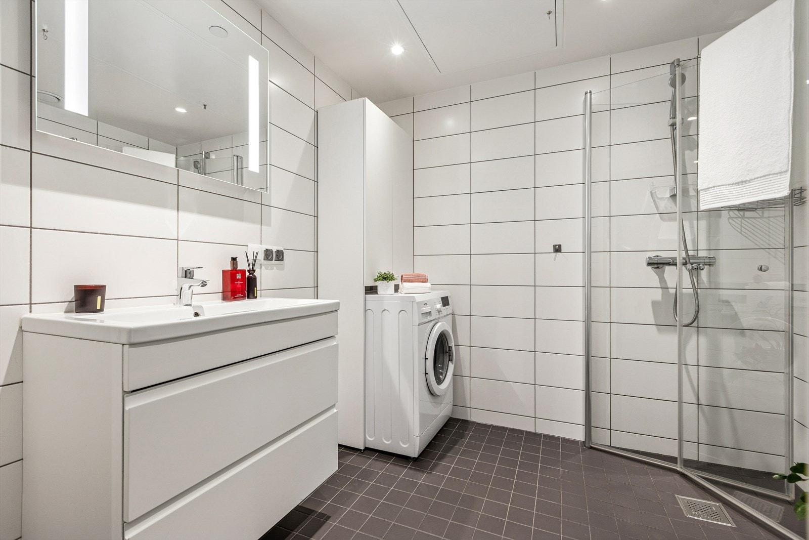 Badet byr på blant annet innfellbare dusjvegger, vegghengt klosett, servant og opplegg for vaskemaskin med tilhørende lagringsplass Galleribilde