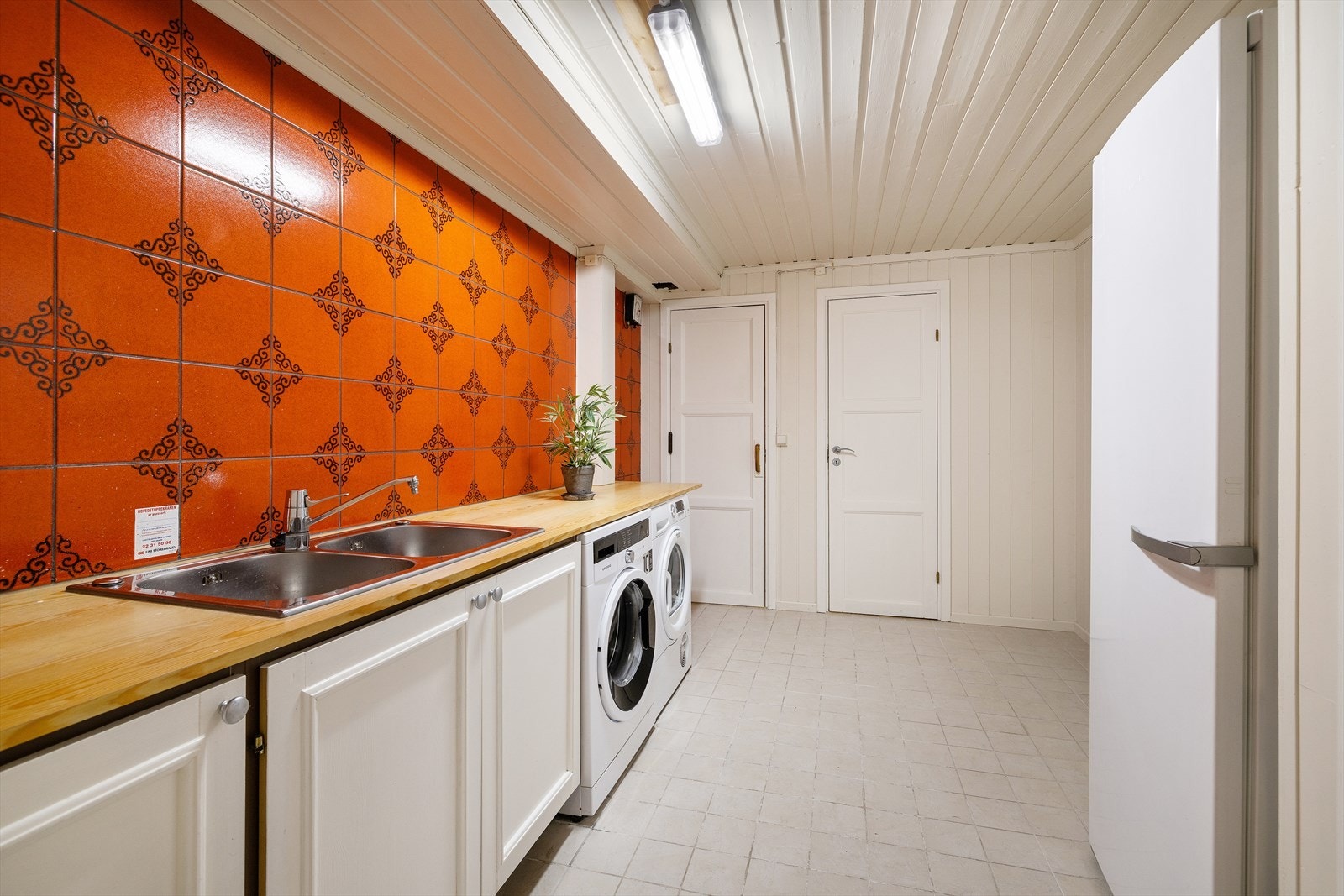 Praktisk innredet vaskerom i underetasjen med eldre innredning som har montert skyllekar og opplegg for vaskemaskin. Galleribilde