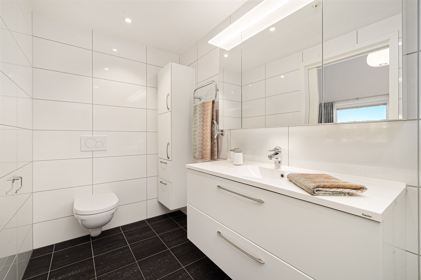 Baderommet har servant over skuffinnredning og speilskap med belysning. Tilhørende vegghengt høyskap med god oppbevaringsplass. Dusjnisje med glassdører og vegghengt toalett Galleribilde