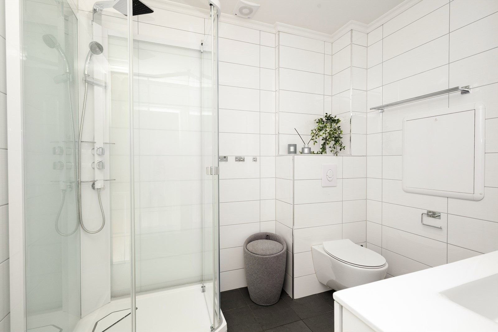 Badet er innredet med veggmontert toalett, dusjkabinett og servantinnredning med skuffer, speil og veggmontert høyskap. Galleribilde