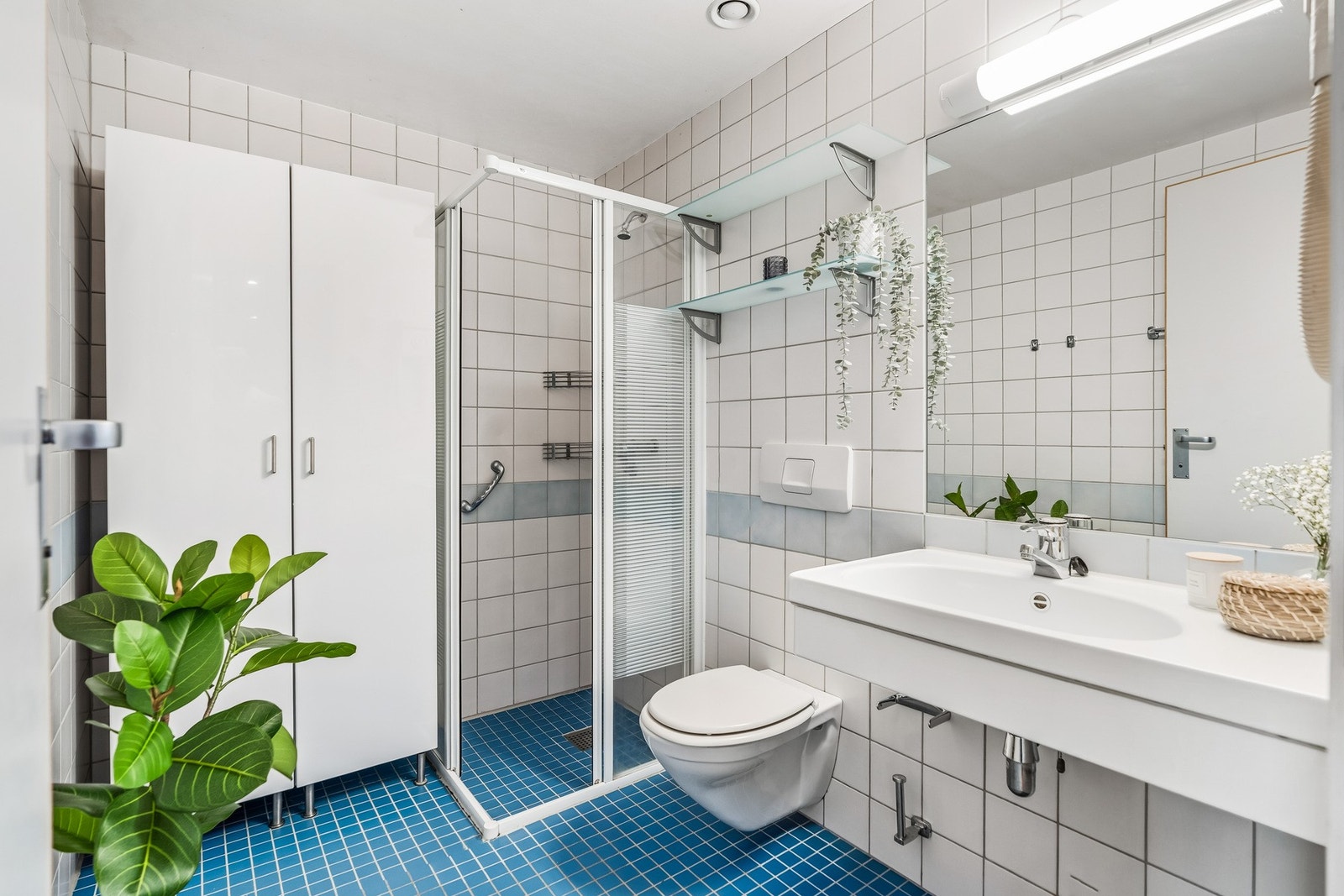 Badet har god størrelse og består av vegghengt toalett, servant og dusjhjørne. Plass til skap eller annen innredning til oppbevaring. Elektriske varmekabler i gulv. Tidløse fliser på vegger og gulv. Galleribilde