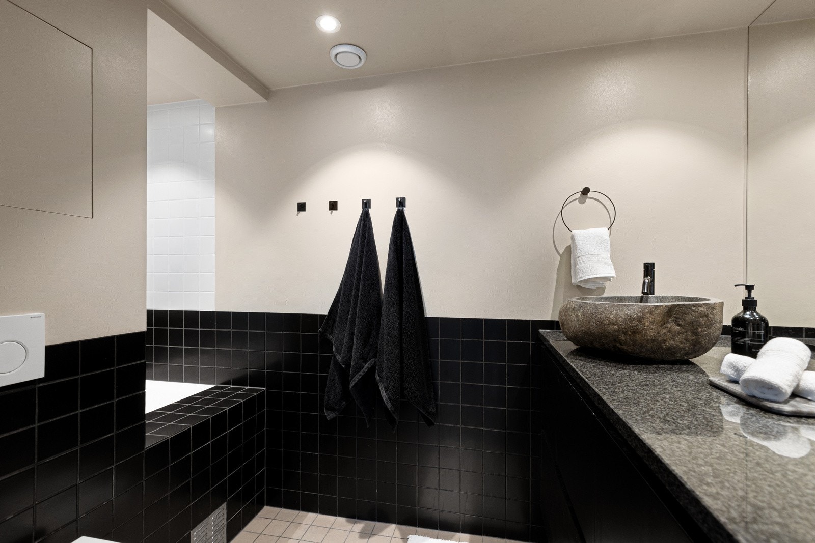 Badet er delikat utført med flislagte gulv og veggflater, kombinert med enkelte malte veggflater og hvitmalt, slett himling. Rommet har en stilren og gjennomført utforming med behagelig gulvvarme og innfelte spotlights som gir godt og jevnt lys. Galleribilde