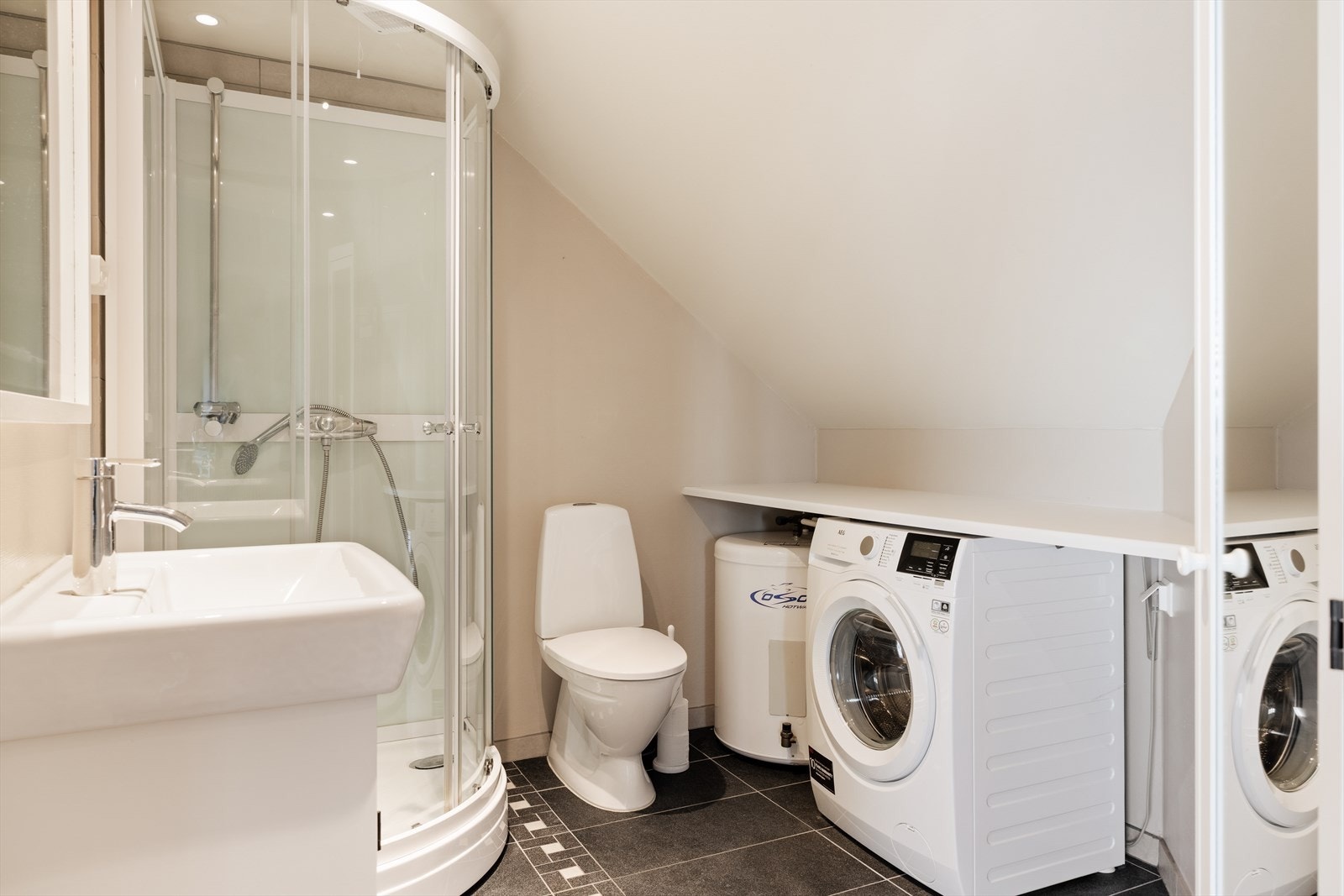 Bad fra ca. 2003 med flislagt gulv og varmekabler. Veggene har malte plater og taket er malt. Rommet er utstyrt med servant i innredning, toalett, dusjkabinett og opplegg for vaskemaskin. Galleribilde