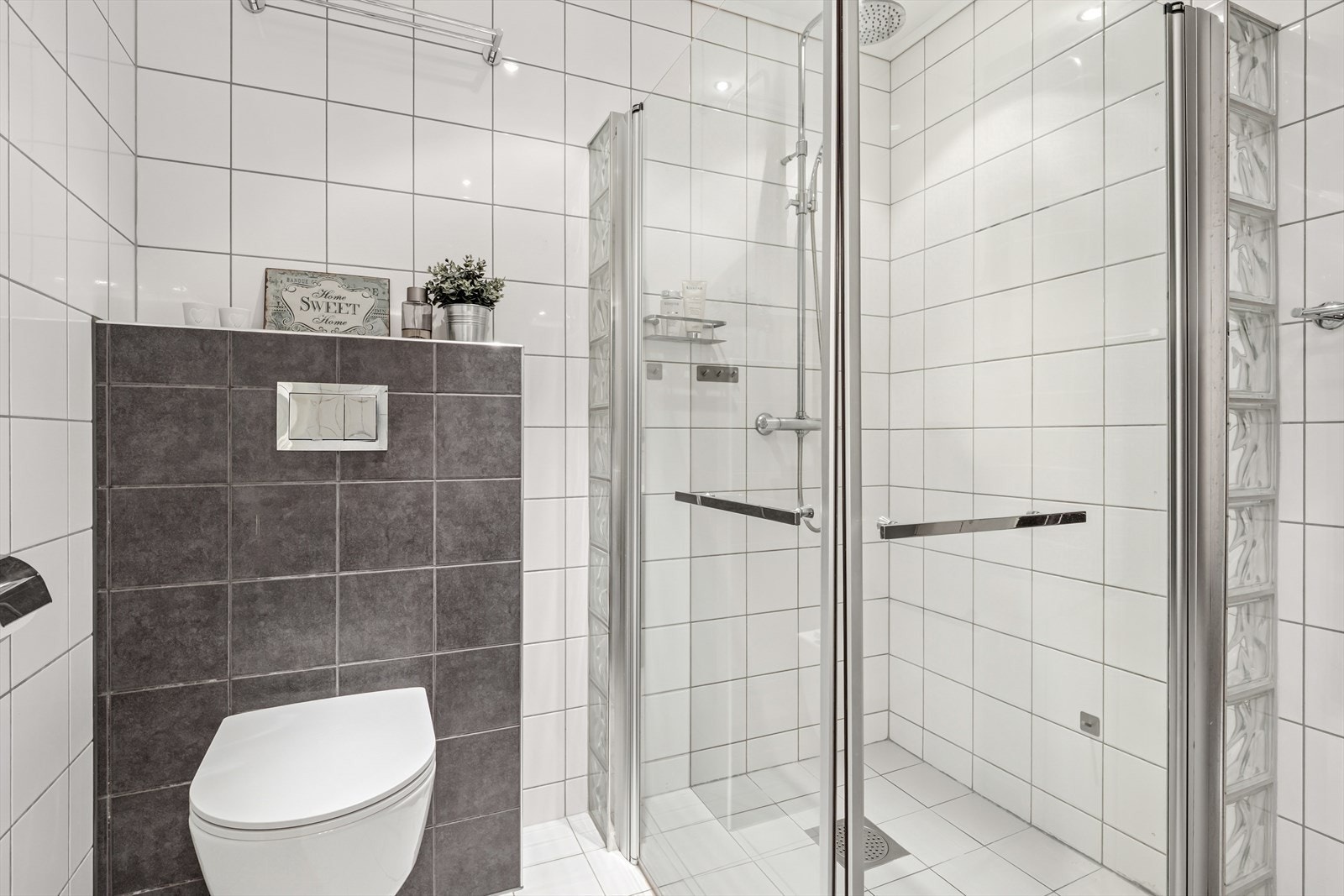 Rommet er utstyrt med en innredning som inkluderer en nedfelt servant, veggmontert toalett og dusjvegger i hjørnet. Galleribilde