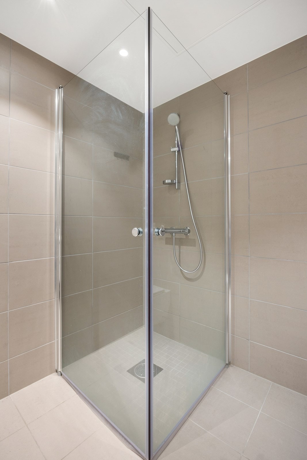 Romslig dusjhjørne med inn-/utadslående dører i herdet glass. Galleribilde