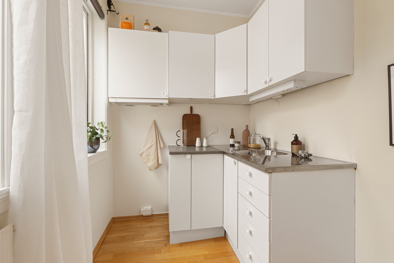 Kjøkkeninnredning fra 2015 med hvite glatte fronter. Mørk laminatbenkeplate og benkeplate beslått i rustfritt stål med innfelt vaskekum og ettgreps krummet armatur fra Oras Galleribilde