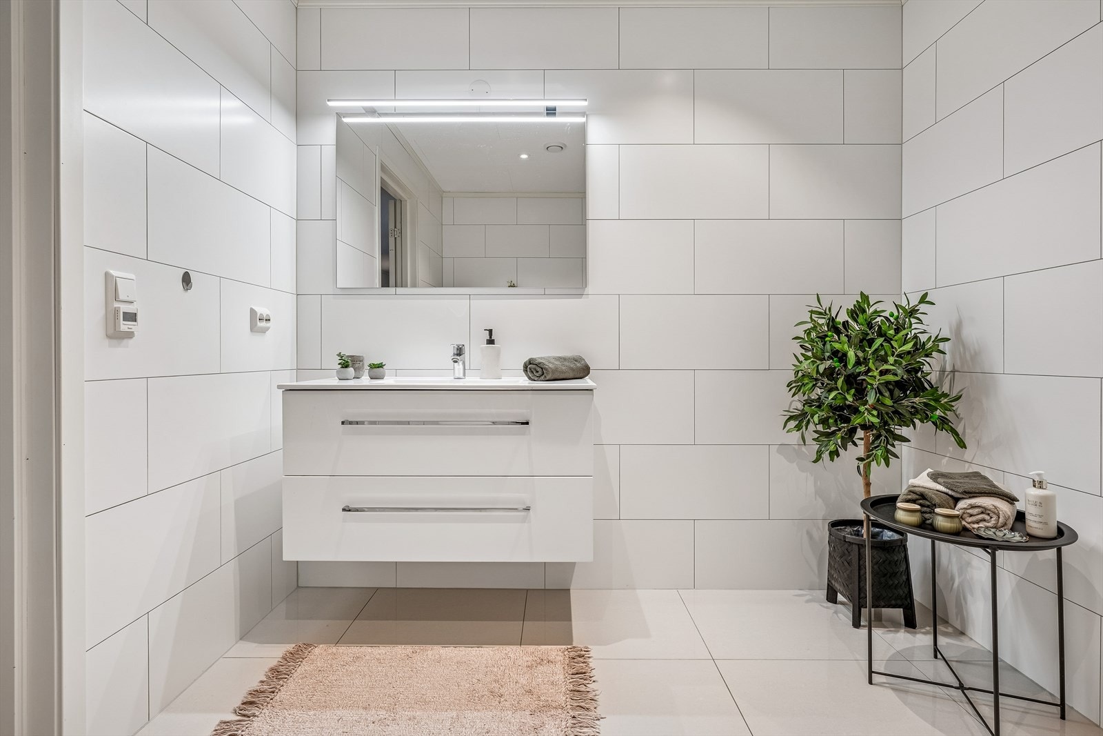 Delikat, flislagt bad med servantskap, speil med belysning og vegghengt toalett. Galleribilde