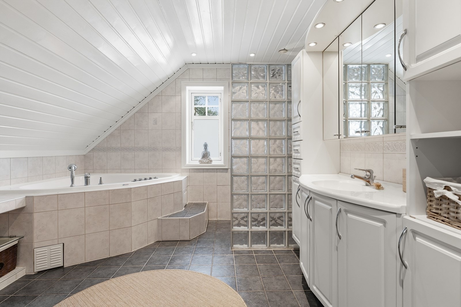 Romslig flislagt badeværelse med badekar, dusjhjørne, wc og servant. Galleribilde