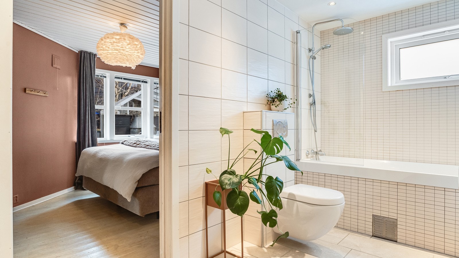 Badet er innredet med en stilig skuffeseksjon med servant, vegghengt toalett og et stilig badekar med dusj kledd i mosaikkfliser. Fra badet er det direkte adgang til soverommet. Galleribilde