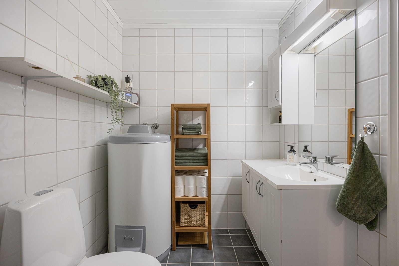 Badet er innredet med hvite veggfliser og mørke gulvfliser. Galleribilde