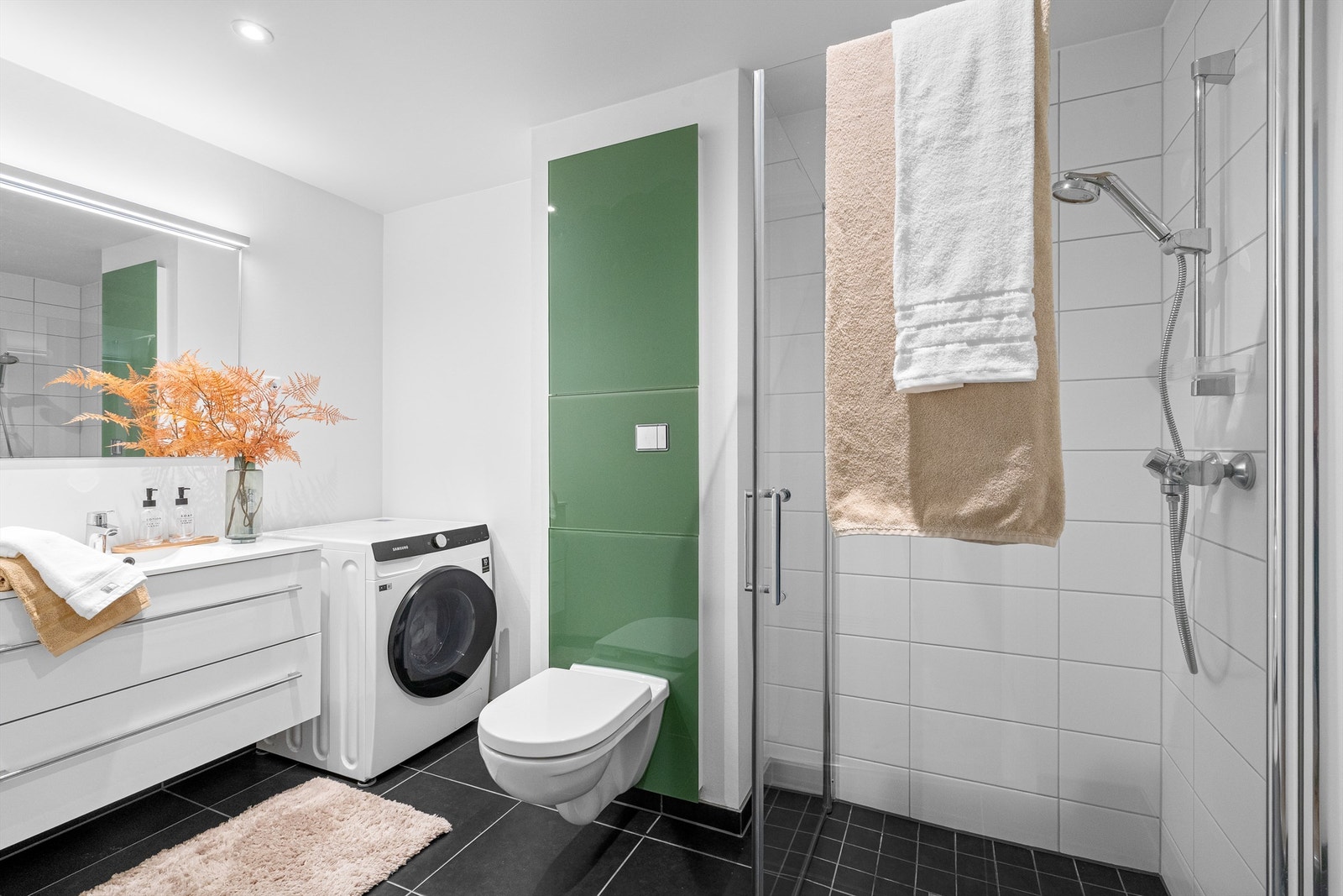 Fint bad av godt størrelse med varme i gulv, fliser på gulv og i dusjsone. Det er dusjhjørne med innfellbare dører, vegghengt toalett og servant med oppbevaringsplass i skuffer. Stort speil på vegg. Galleribilde