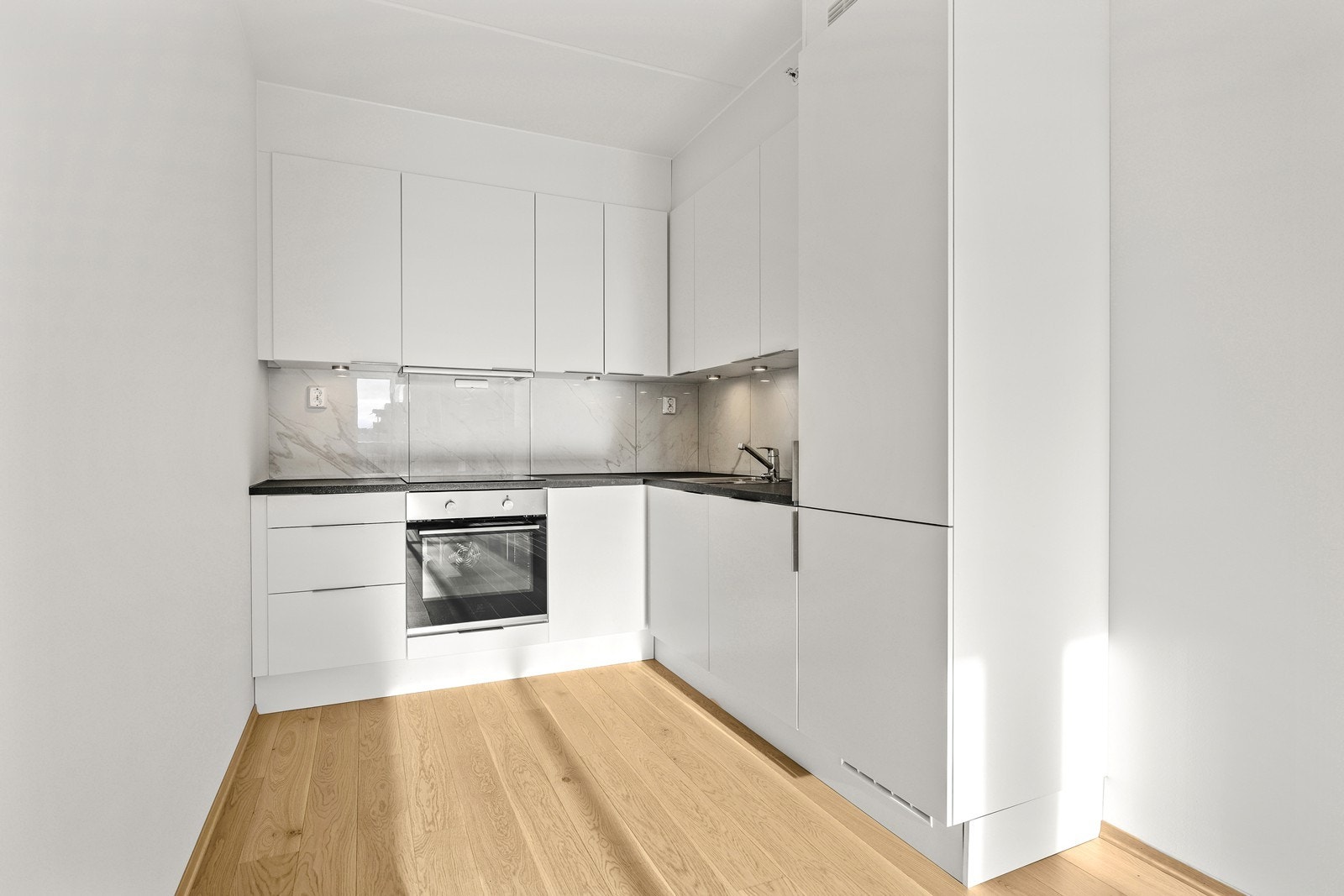 Kjøkkeninnredning fra Norema med slette, hvite fronter og mørk laminatbenkeplate. Galleribilde