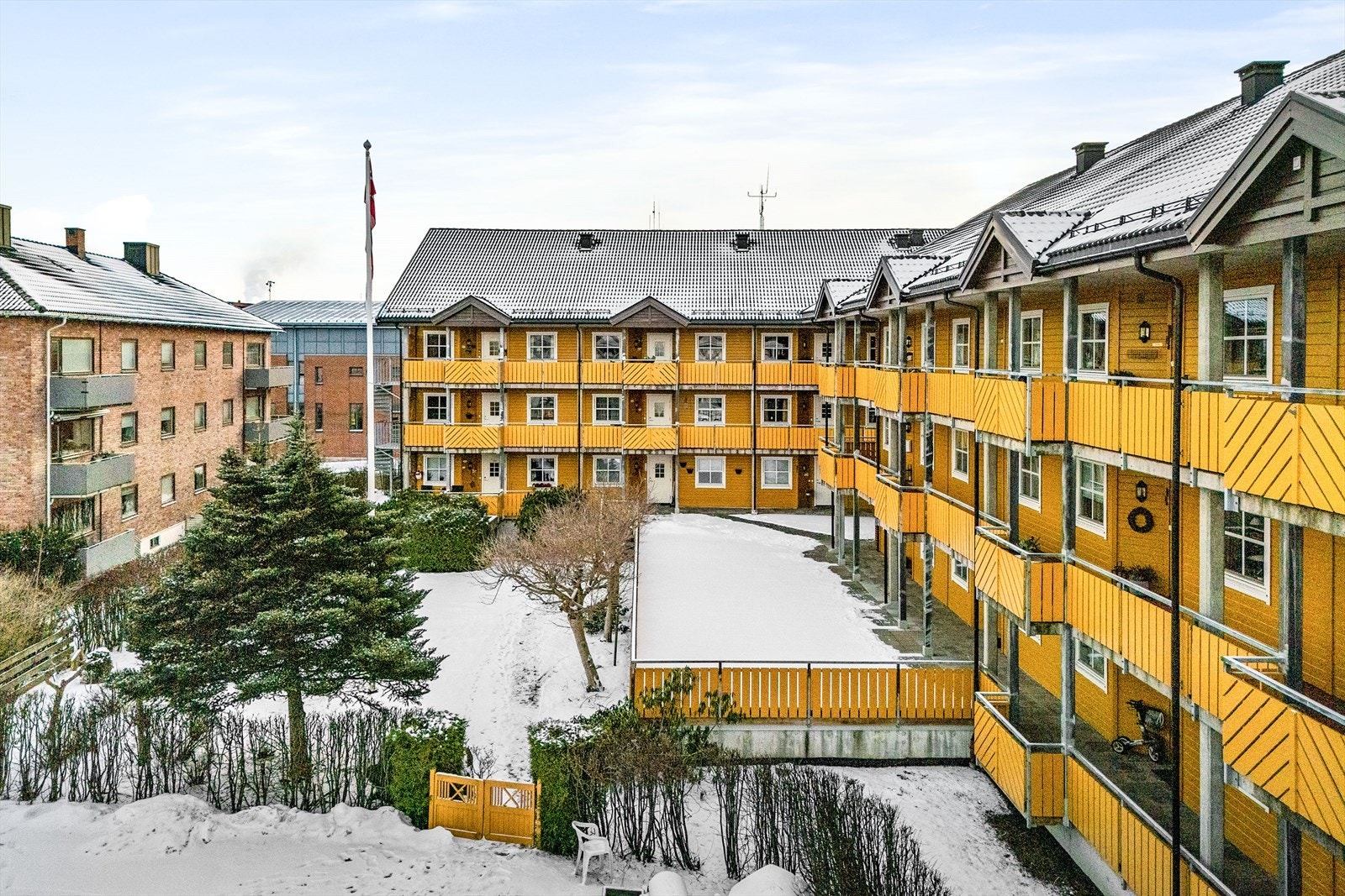 Bygårdens bakside danner en fin bakgård med skjermede fellesarealer og hage. Den er delt i to- en stor hellelagt plass som bare venter på å bli møblert med sittebenker. Ned en liten trapp utenfor rekkverket, åpner det seg en velfrisert, beplantet hage. Galleribilde