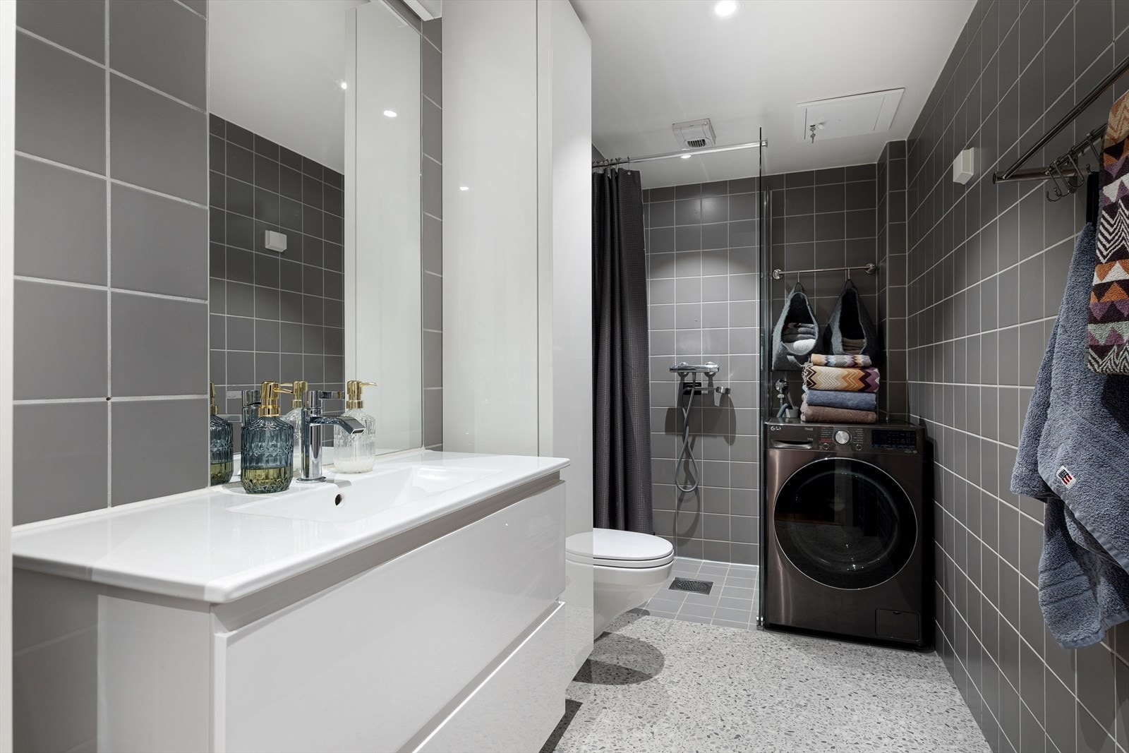 Moderne, flislagt baderom med downlights i himlingen og gulvvarme. Utenfor dusjsonen er det lagt gulvbelegg oppå flisene. Galleribilde