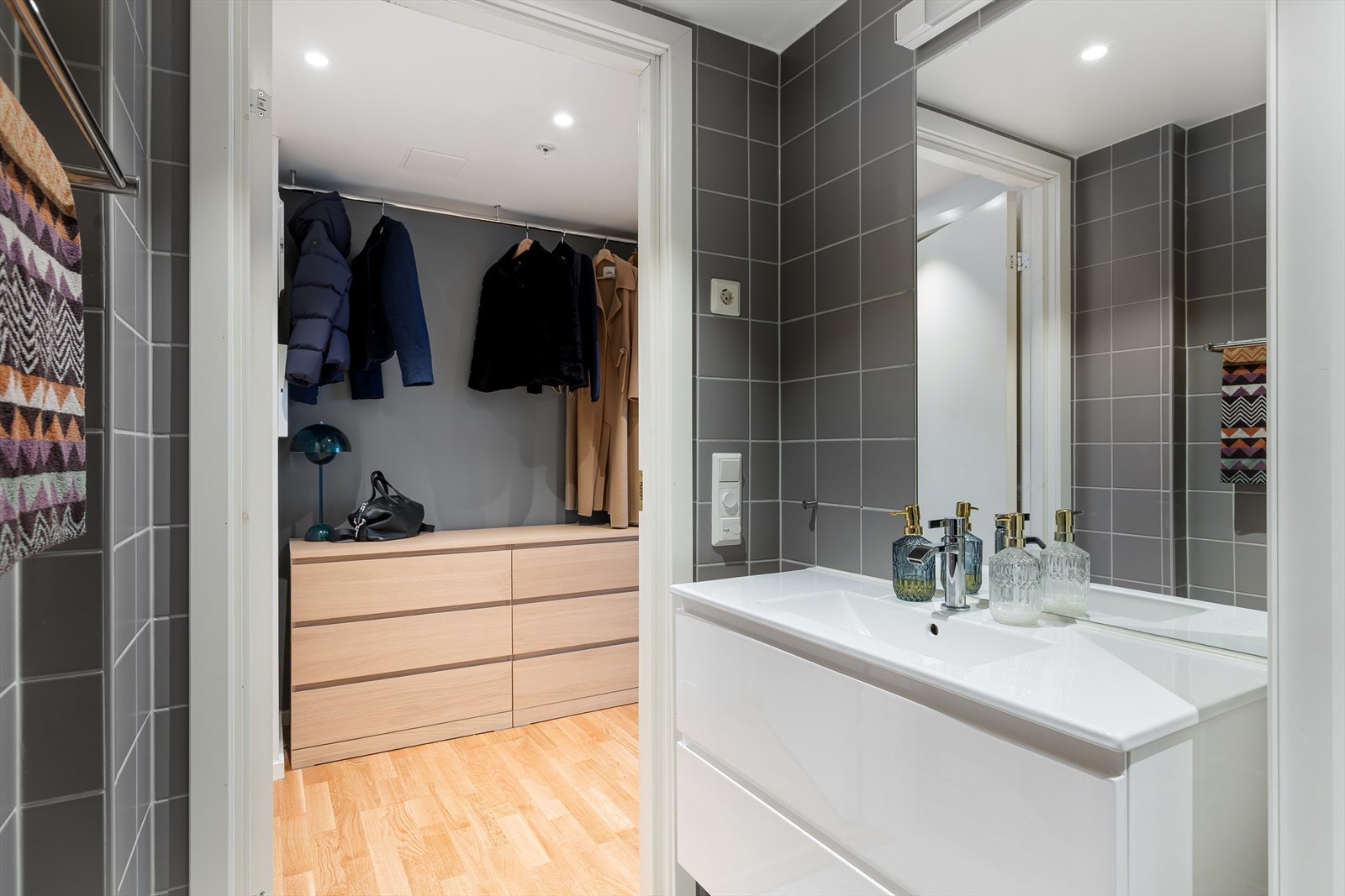 Badet er utstyrt med veggmontert toalett, dusjhjørne med vegg og dør i herdet glass, servant med underskap, speil og belysning samt opplegg for vaskemaskin. Galleribilde