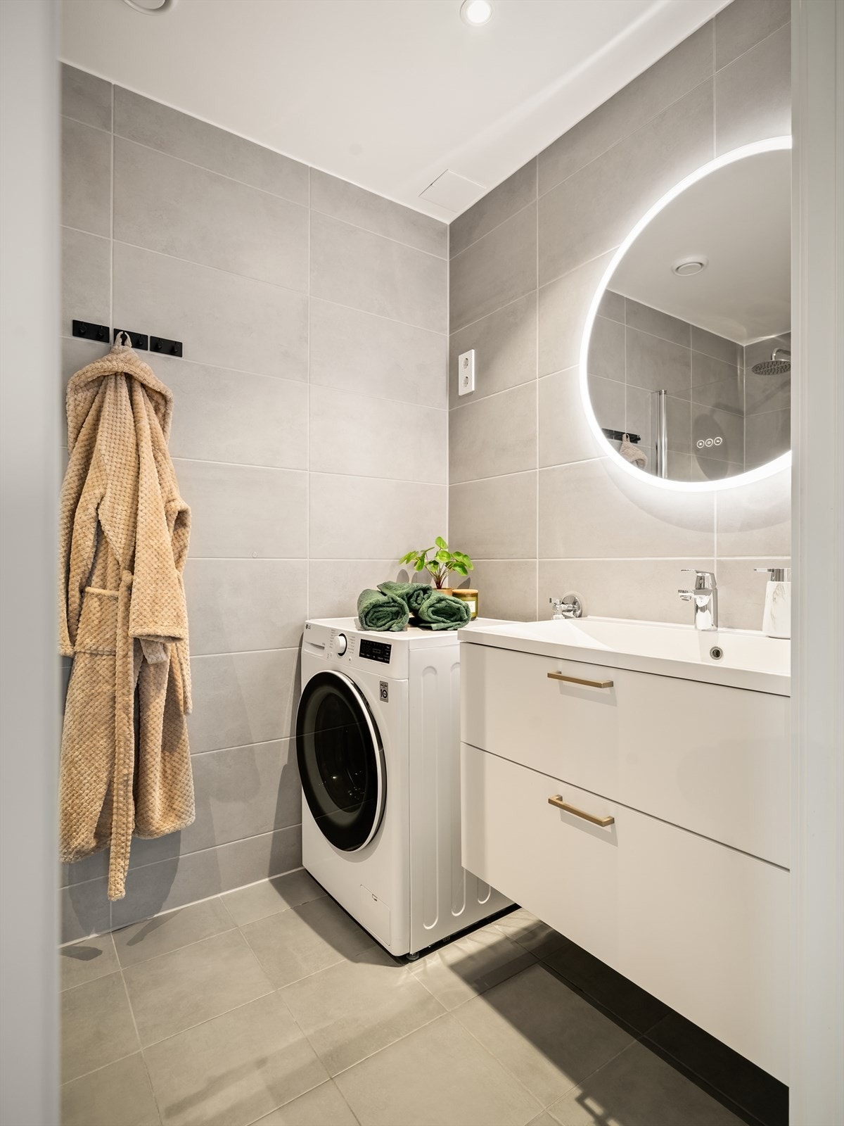 Bad med flislagte overflater, servantinnredning og opplegg for vaskemaskin. Galleribilde