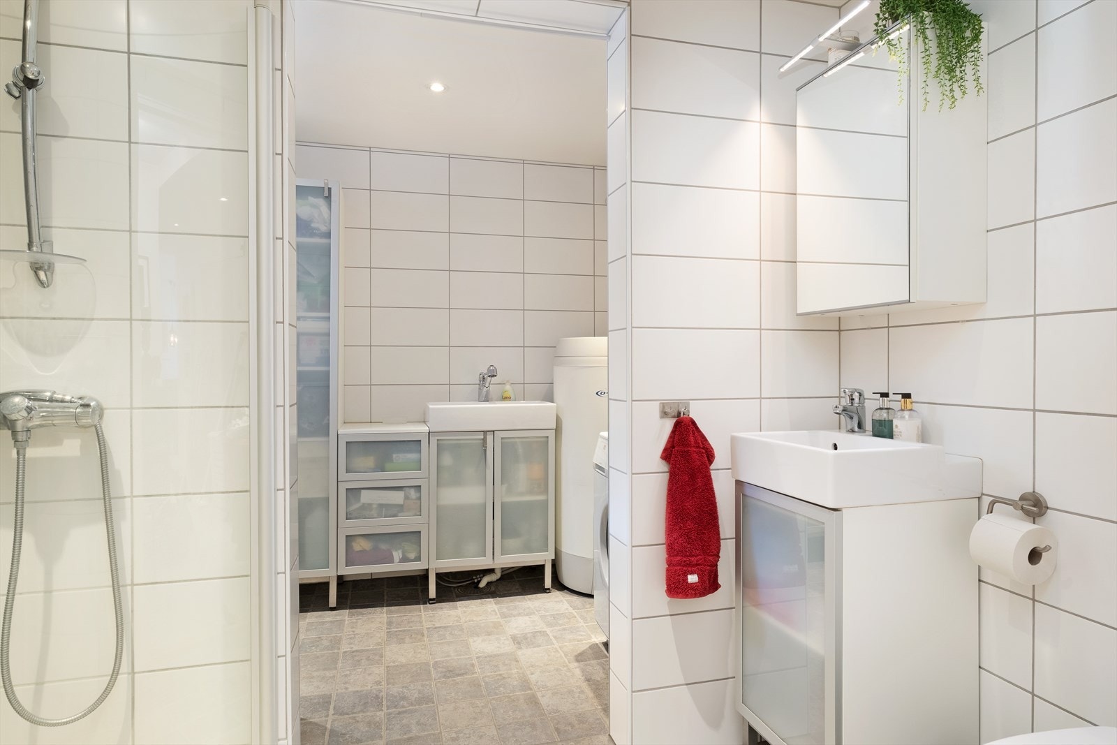 Like ved inngangen ligg eit heilflisa bad som inneheld dusjhjørne, veggmontert toalett, nedfelt servant med underskåp og spegel. Galleribilde