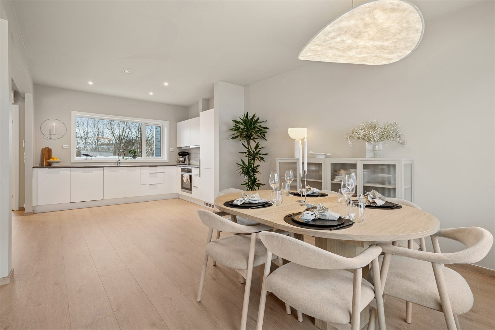 Kjøkkenet er stilrent med hvite glatte fronter, laminert benkeplate med nedfelt kjøkkenvask og fliser på vegg over benk Galleribilde