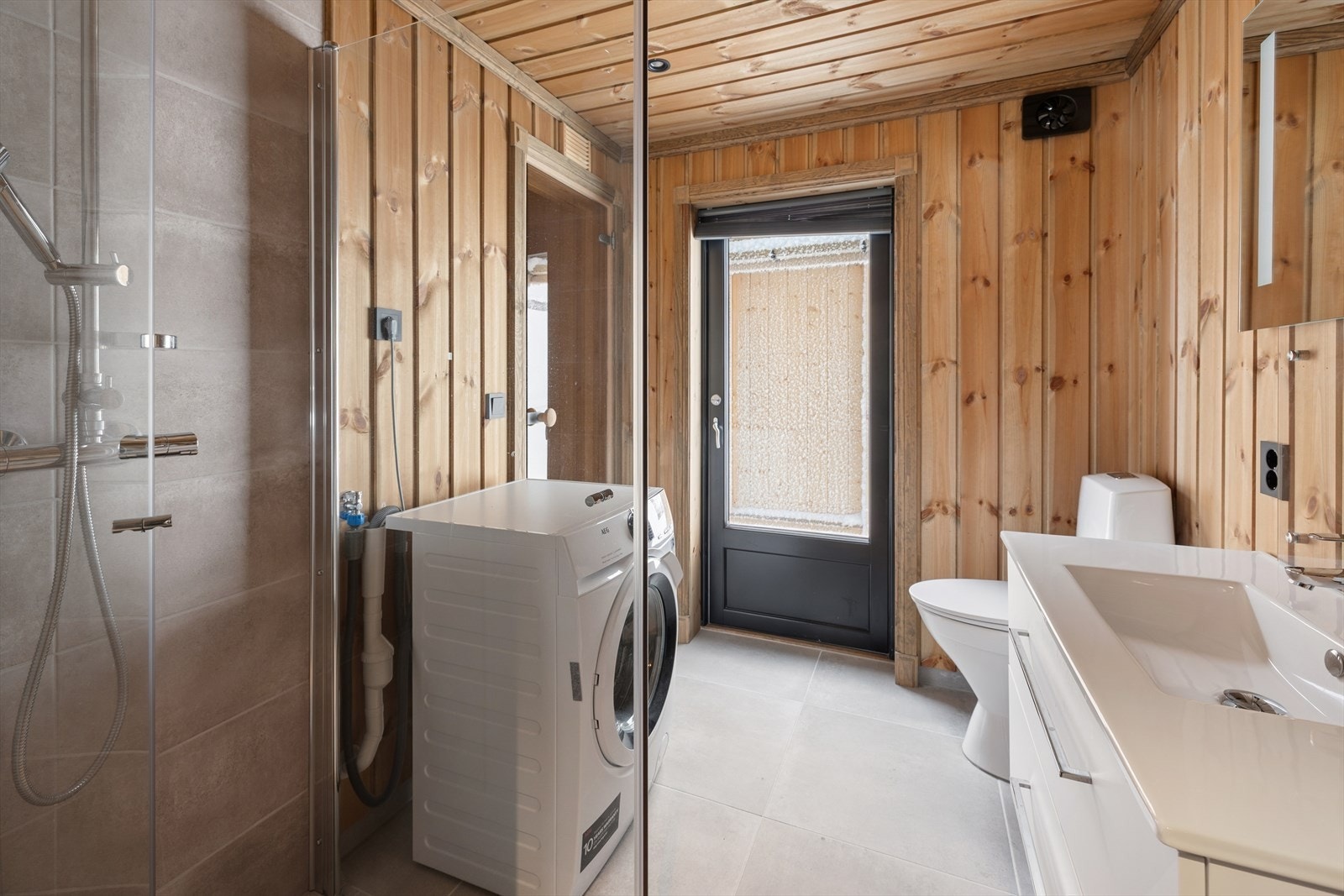 Badet er utstyrt med innredning med nedfelt servant, toalett, dusjhjørne med glassvegger og opplegg for vaskemaskin. Galleribilde