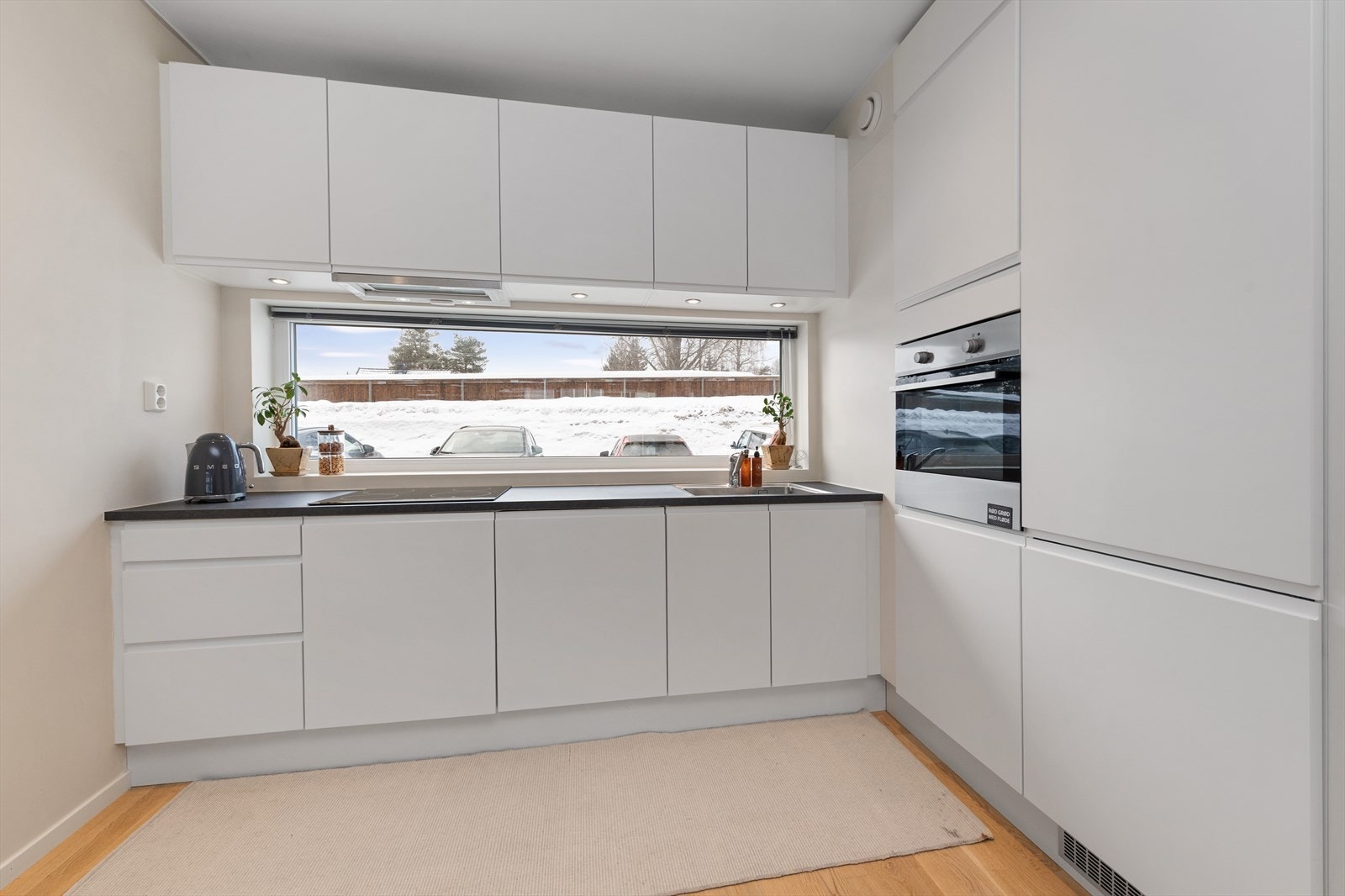 Lyst og moderne kjøkken med integrerte hvitevarer som kjøle-/fryseskap, oppvaskmaskin, stekeovn og platetopp Galleribilde