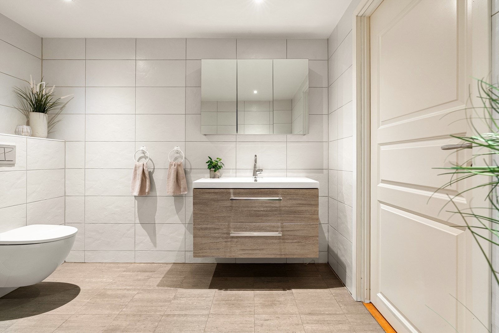 Badet er innredet med servant i møbel, speilskap, vegghengt toalett, dusj med glassdører og opplegg for vaskemaskin. Galleribilde