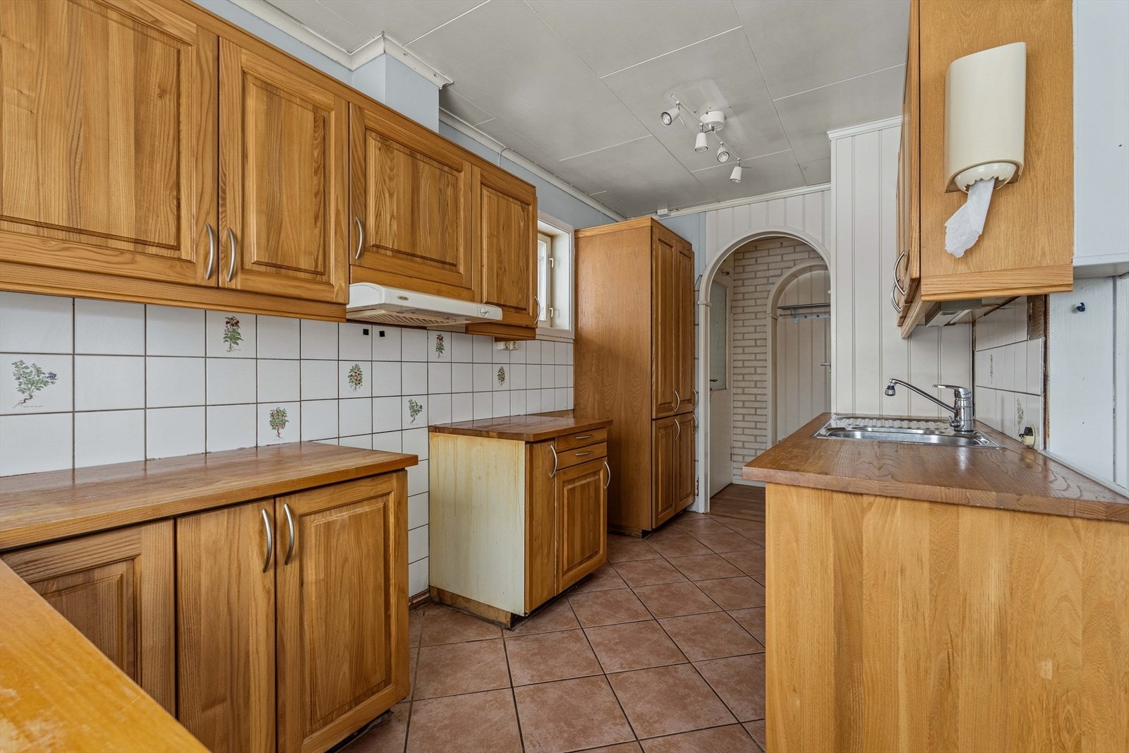 Kjøkkenet har en praktisk og funksjonell utforming med gode benke- og skapflater som gir rikelig med oppbevaringsplass. Rommet har lysinnslipp fra vinduet over benken og en gjennomgående planløsning som gjør det mulig å bevege seg mellom arbeidsstasjonene Galleribilde