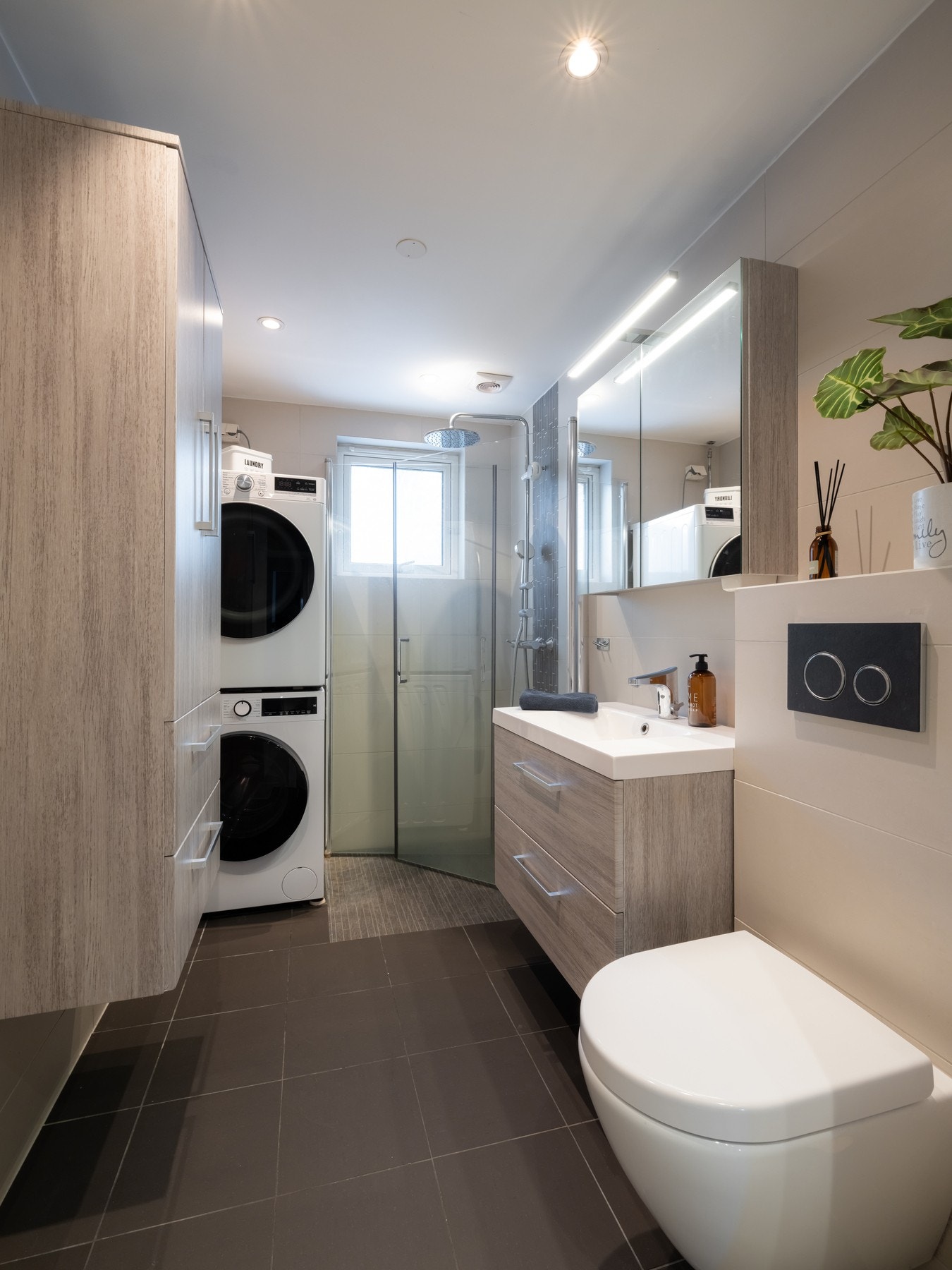 Badet inneholder vegghengt innredning med skuffer og heldekkende servant, speilskap med overbelysning, vegghengt wc og dusjhjørne med innfellbare dører og regnfallsdusj. Galleribilde