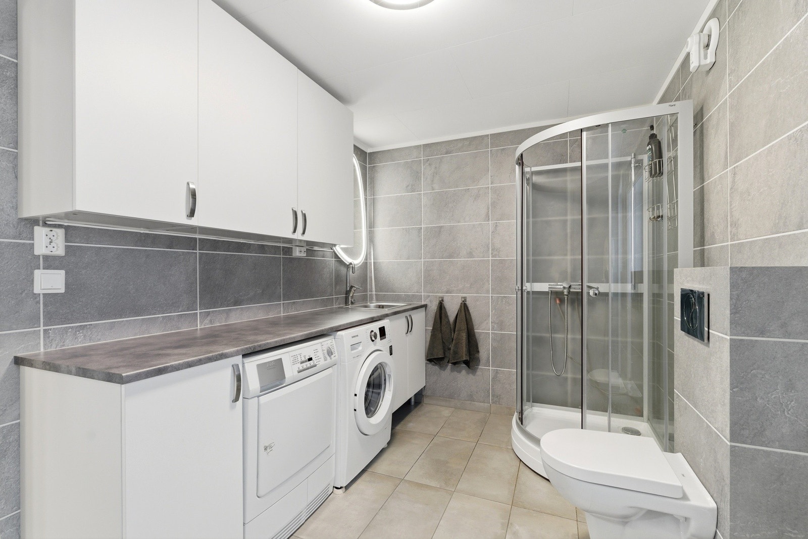 Flott bad/vaskerom, modernisert i 2018 - utstyrt med nedfelt skyllekar, veggmontert toalett, dusjkabinett og opplegg for vaskemaskin. Galleribilde