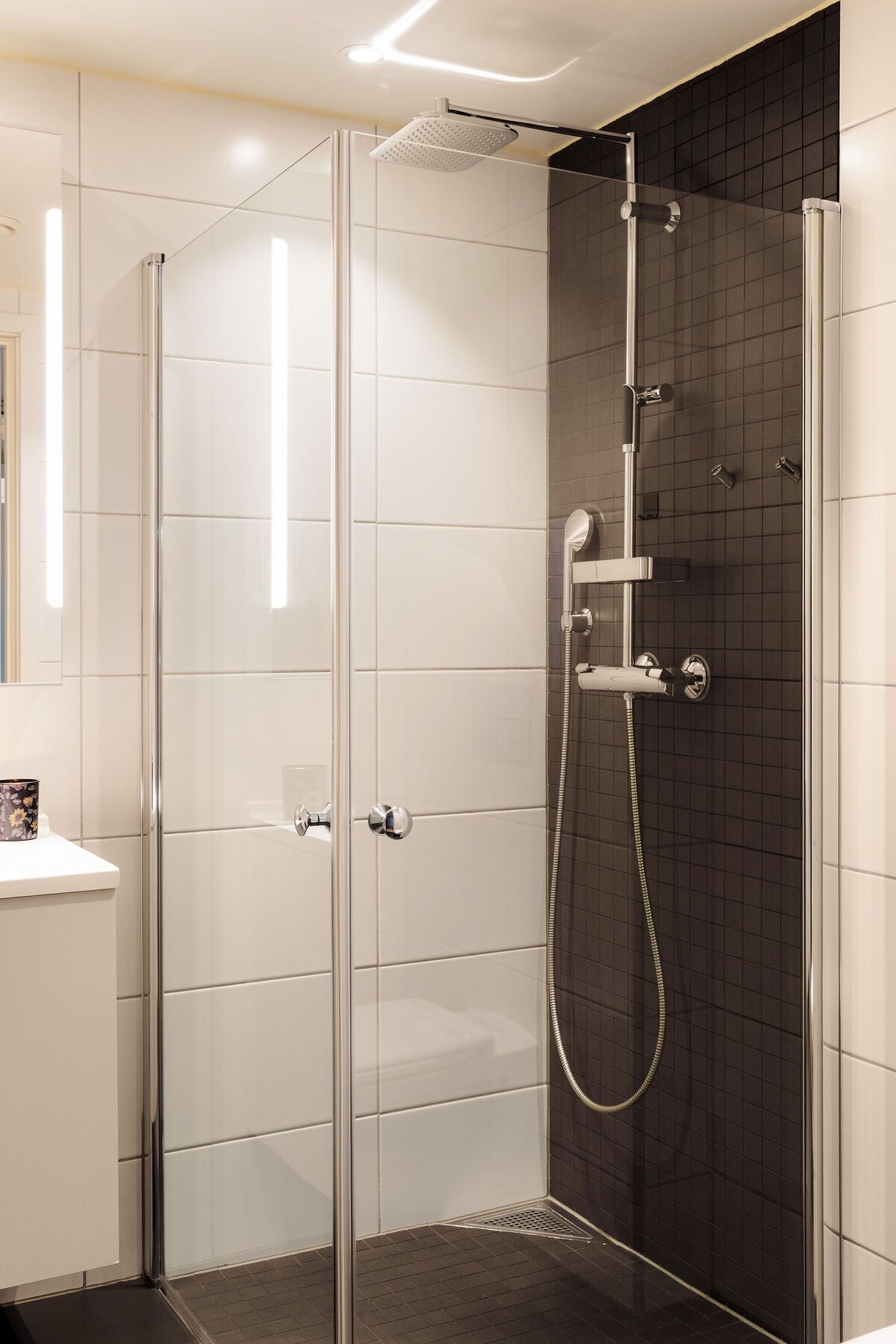 Videre finnes vegghengt toalett med innebygget sisterne og en nedsenket dusjsone med innfellbare glassdører, utstyrt med både hånddusj og regndusj for ekstra komfort. Galleribilde