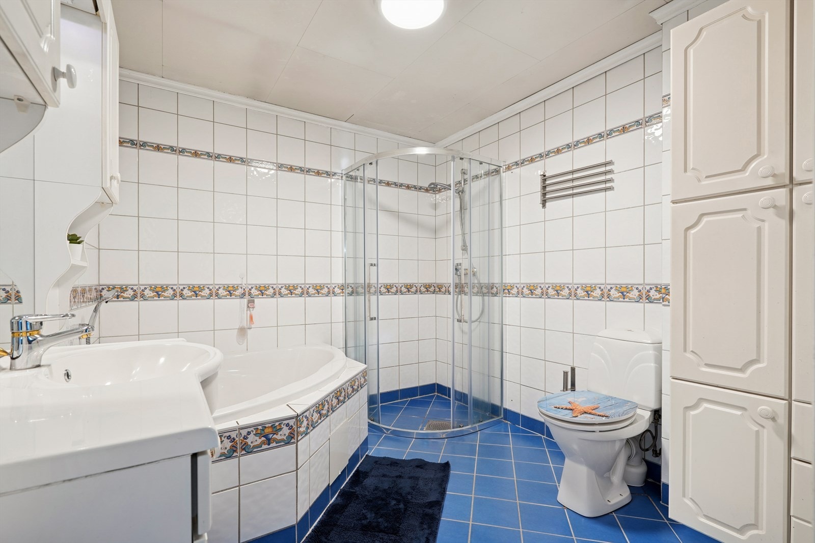 Speil og belysning over servant. Servant i helstøpt plate, hjørnebadekar, dusj med faste felt og dører i herdet glass og gulvstående klosett. Galleribilde