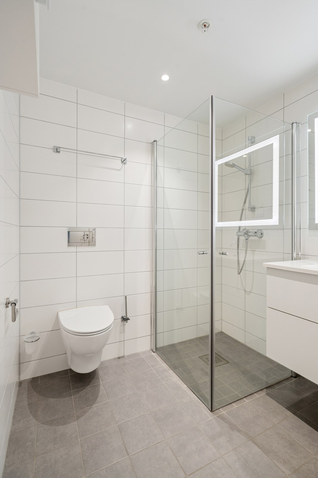 Badet er utstyrt med veggmontert toalett og et stilrent dusjhjørne med foldbare dusjdører. Det er også opplegg for vaskemaskin, praktisk plassert innenfor rommet Galleribilde