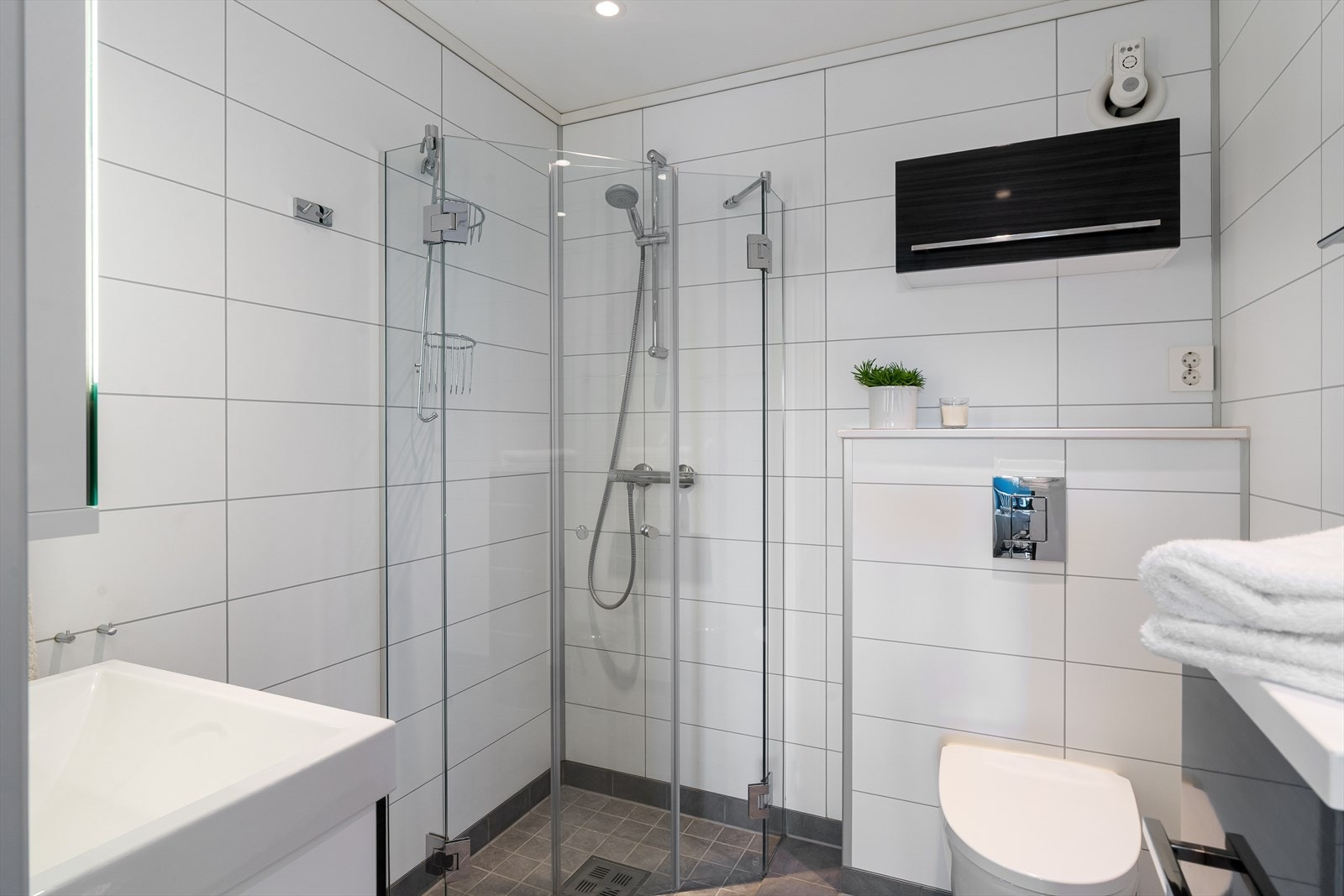 Bad med fliser på gulv som inneholder wc, dusjhjørne, vask i seksjon og varmekabler på gulv. Galleribilde