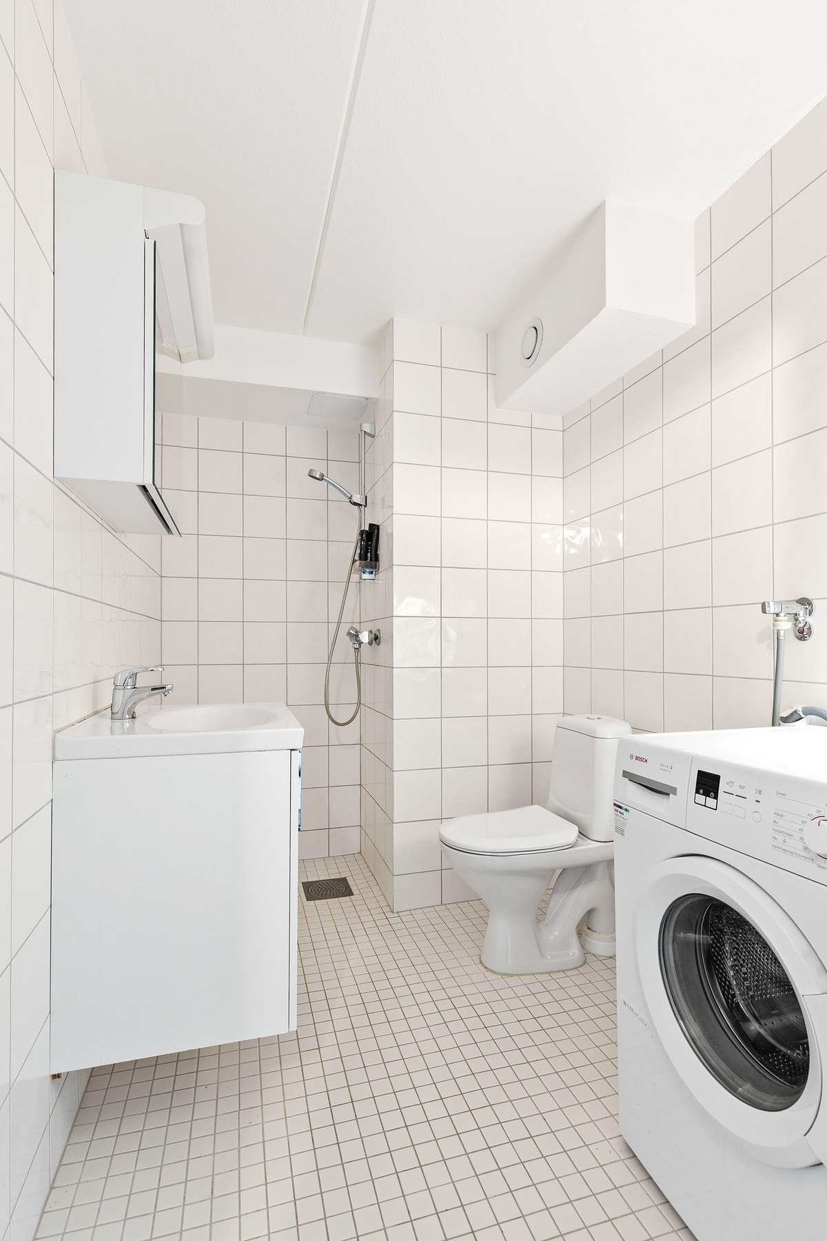 Rommet er innredet med gulvstående toalett, dusjnisje med forheng og servantinnredning med nedsenket vask og speil Galleribilde