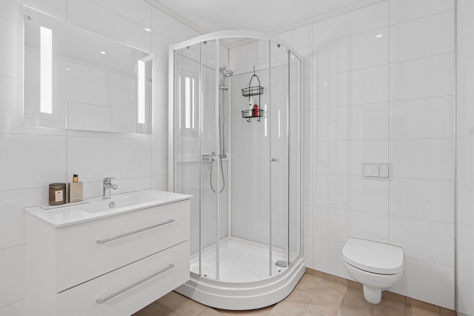 Badet er innredet med en praktisk og stilfull innredning med skuffeseksjon og nedfelt servant, vegghengt speil med belysning, praktisk dusjkabinett og vegghengt toalett. Galleribilde