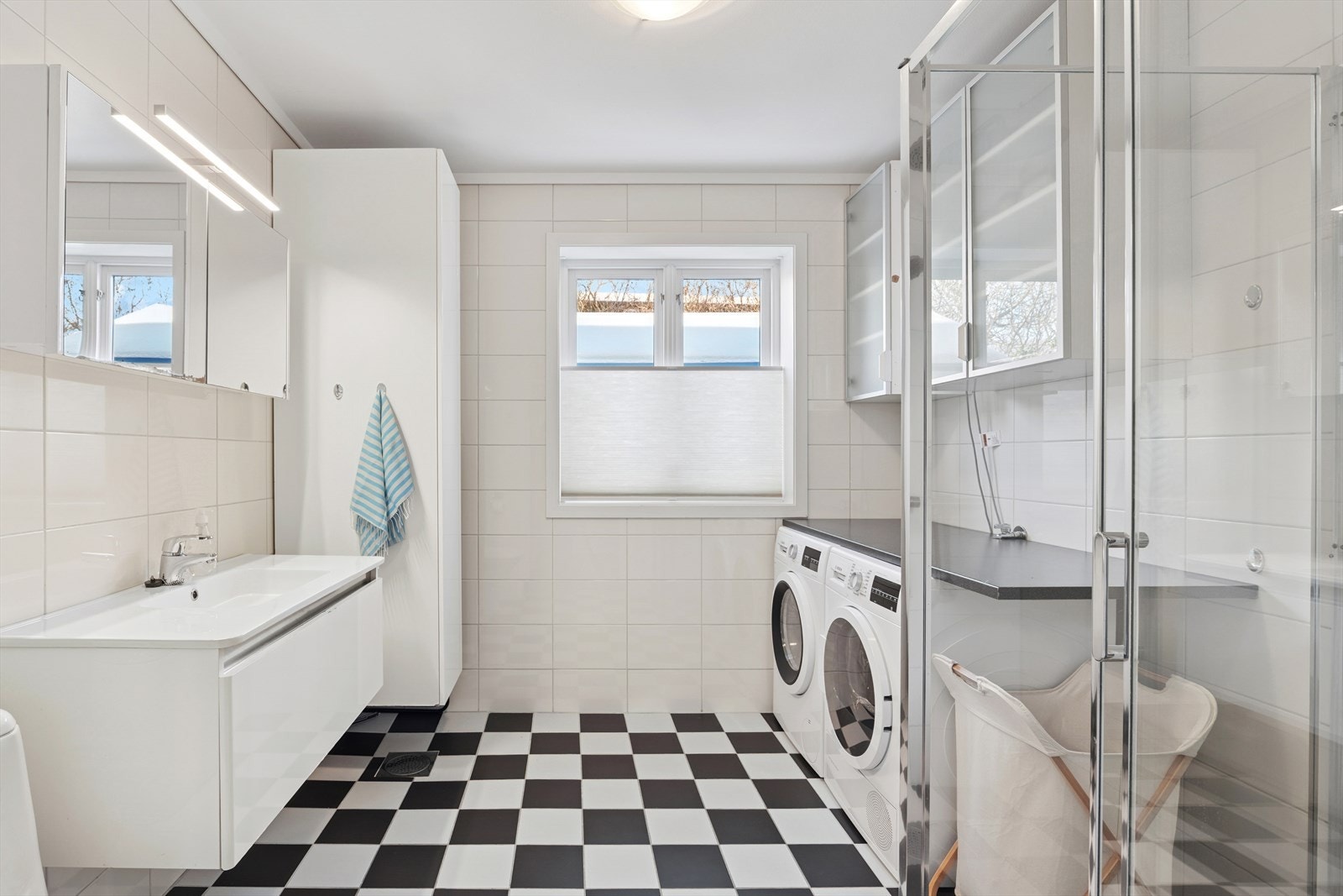 Pent badeværelse med servant, høyskap, dusjhjørne, toalett samt opplegg for vaskemaskin Galleribilde