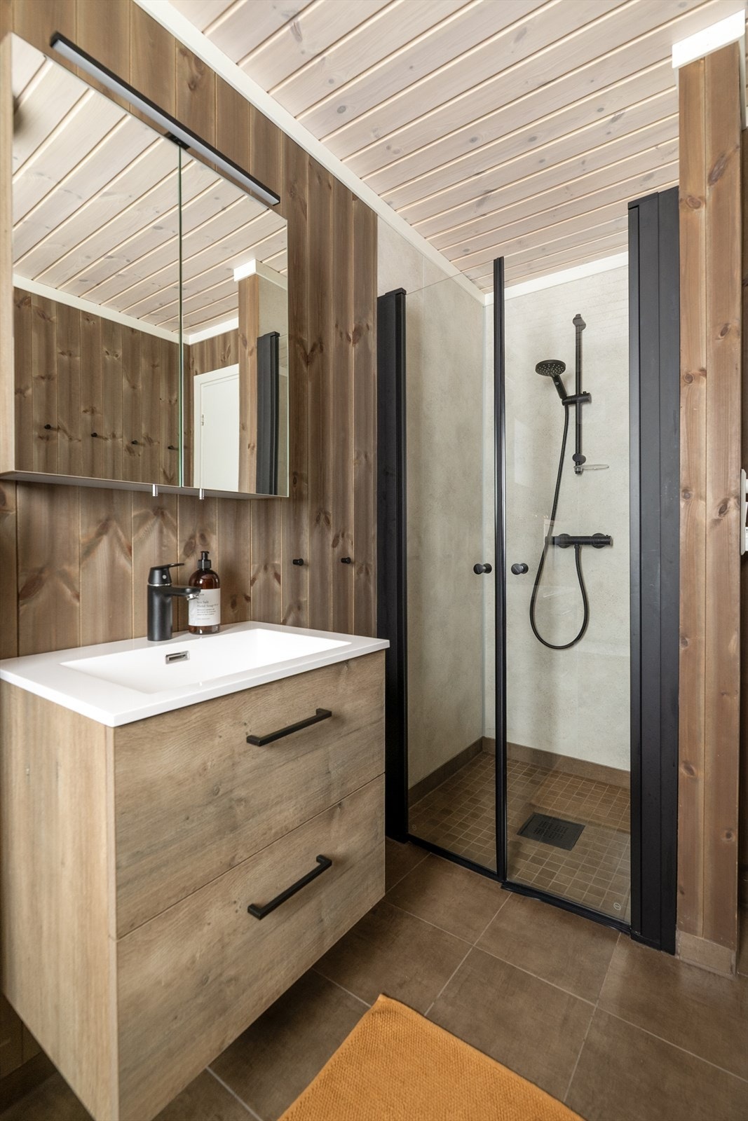 Badet er også innredet med dusjhjørne med glassvegger og sorte profiler, samt sort dusjgarnityr og veggmontert toalett. Galleribilde