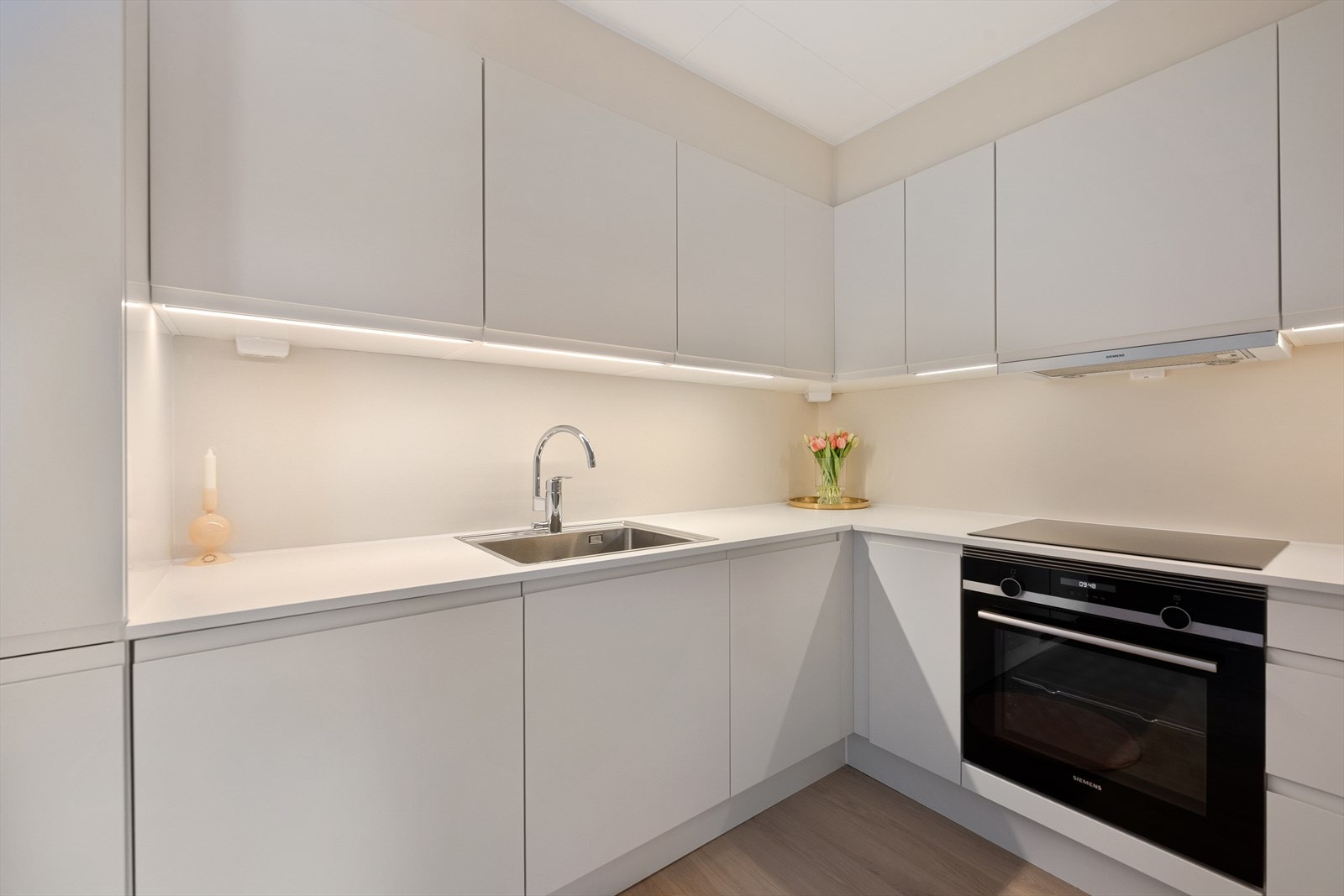 Nytt, delikat og stilrent kjøkken fra 2025 med glatte, hvite fronter og laminat benkeplate med nedfelt kum i rustfritt stål. Galleribilde