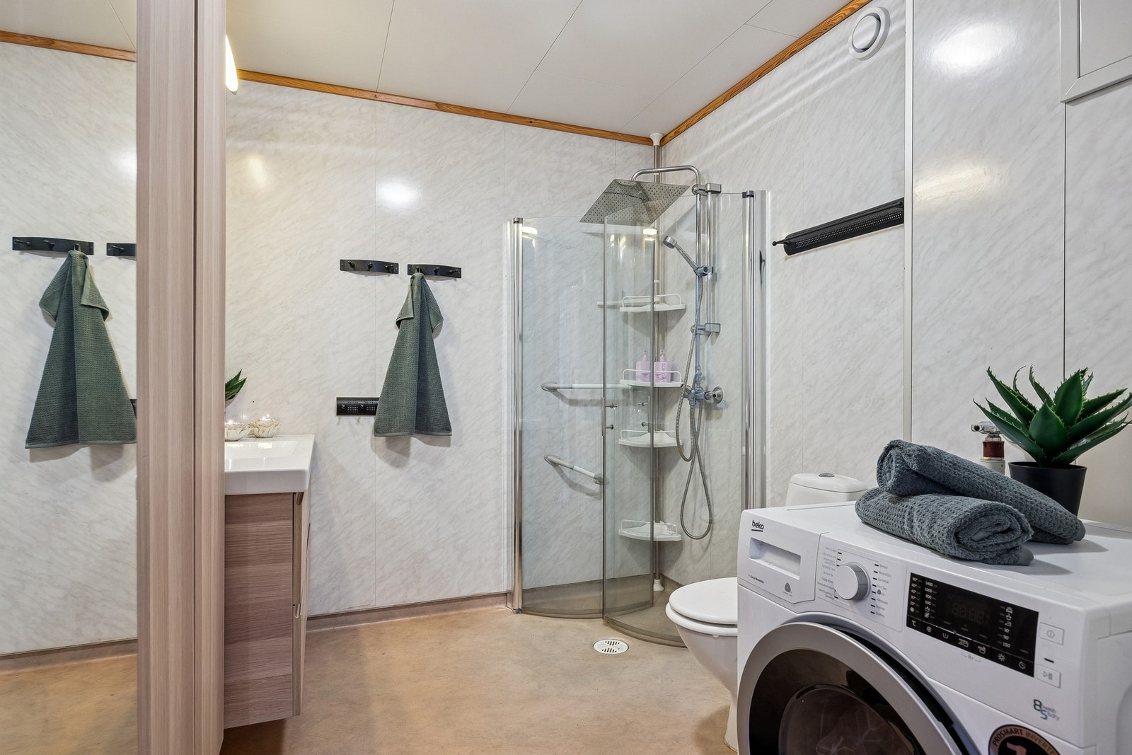 Dusjhjørnet har dører og vegghengt dusjarmatur med både hånddusj og regndusj. Badet har gulvstående toalett og opplegg for vaskemaskin. Galleribilde