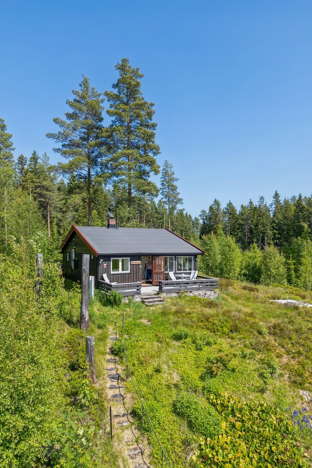 Hytta er plassert høyt i terrenget, med terrengtrapp fra parkeringsplass og adkomst fra privat gutu/veg. Galleribilde