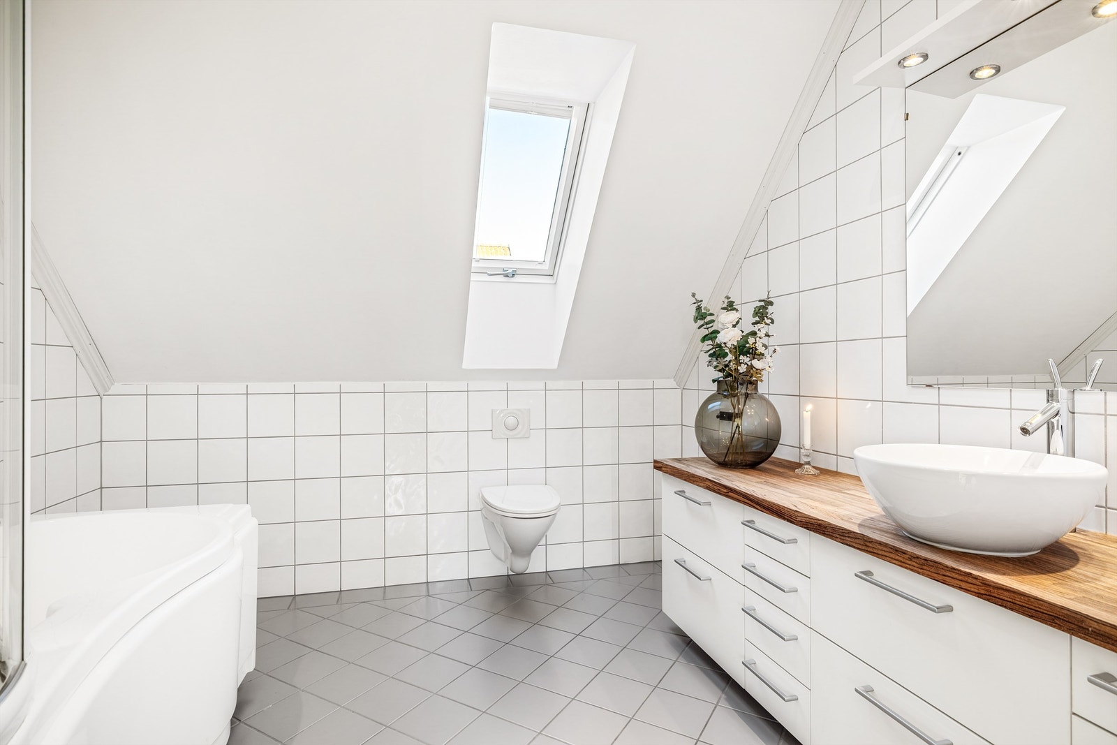 Flislagt bad med takvindu, baderomsinnredning, toalett og badekar med dusjløsning. Galleribilde