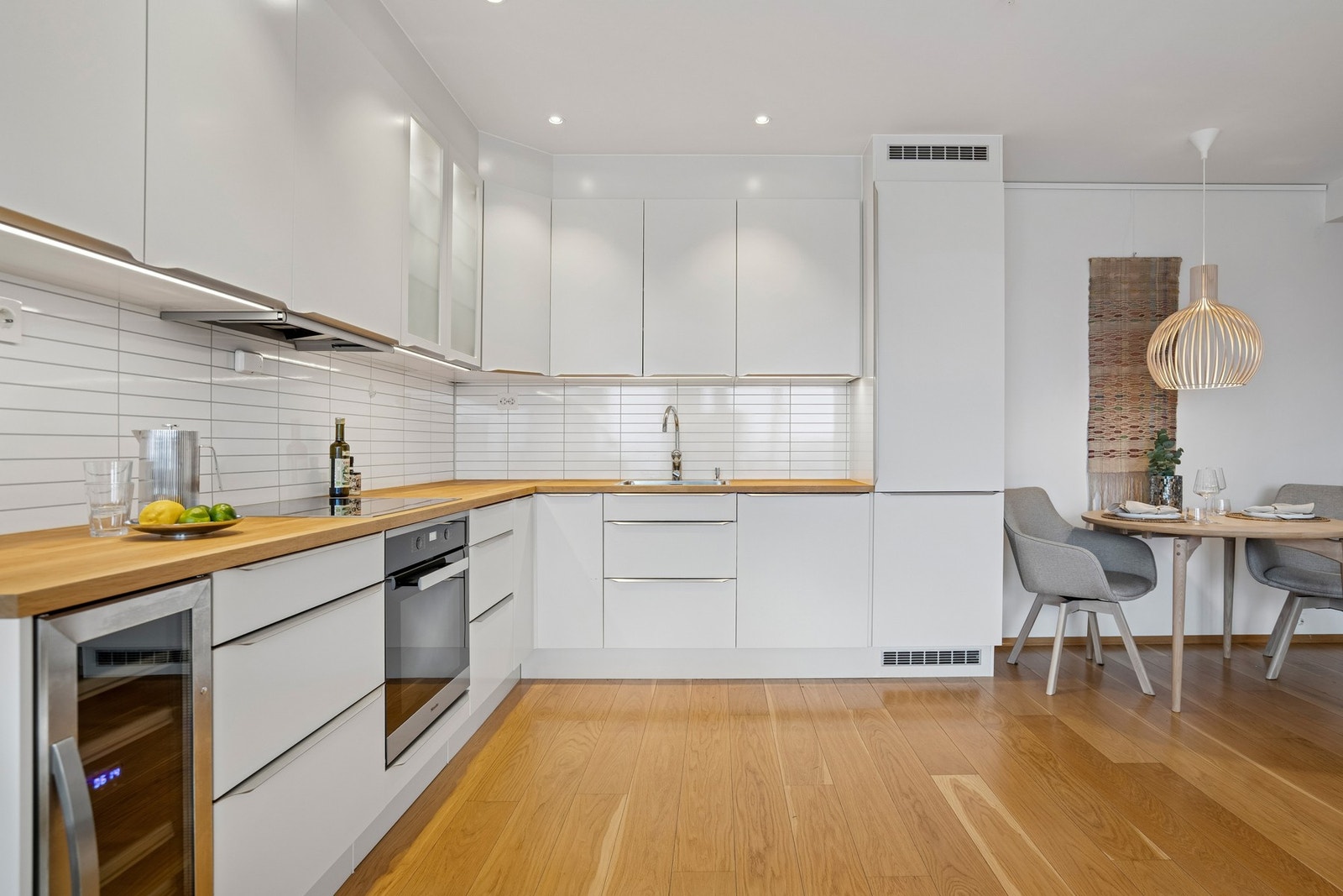 Kjøkken i stilrent hvitt med eikebenk, integrert hvitevarer og vinskap Galleribilde