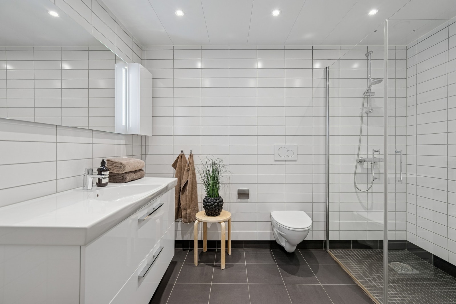 Delikat flislagt bad med vegghengt innredning, stor dusjnisje og spotter i tak Galleribilde