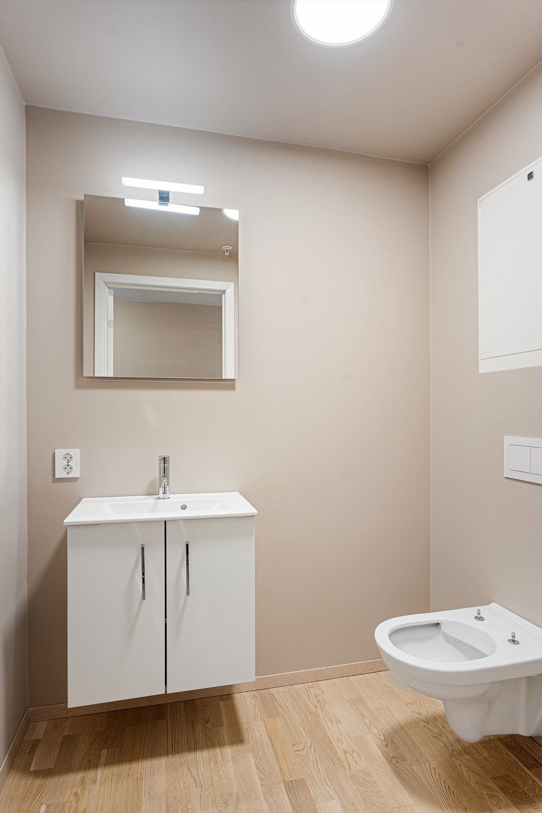Separat WC-rom med parkett på gulv og slette, malte vegger/himling. Rommet har veggmontert toalett og baderomsinnredning med skap og servant. Speil på vegg. Galleribilde