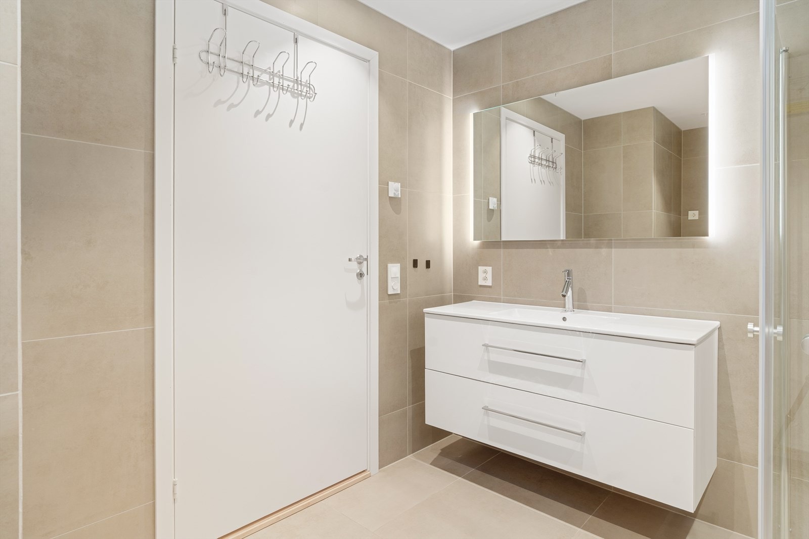 Badet er innredet med dusjhjørne, veggmontert toalett og baderomsinnredning med heldekkende servant. Veggmontert speil med belysning. Galleribilde