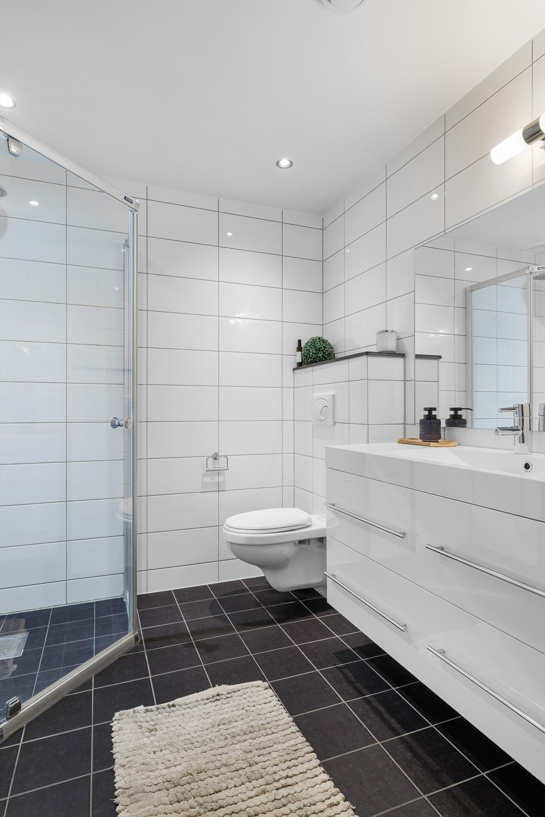 Flott, fliselagt bad med vegghengt wc, dusj og vask i stor seksjon Galleribilde