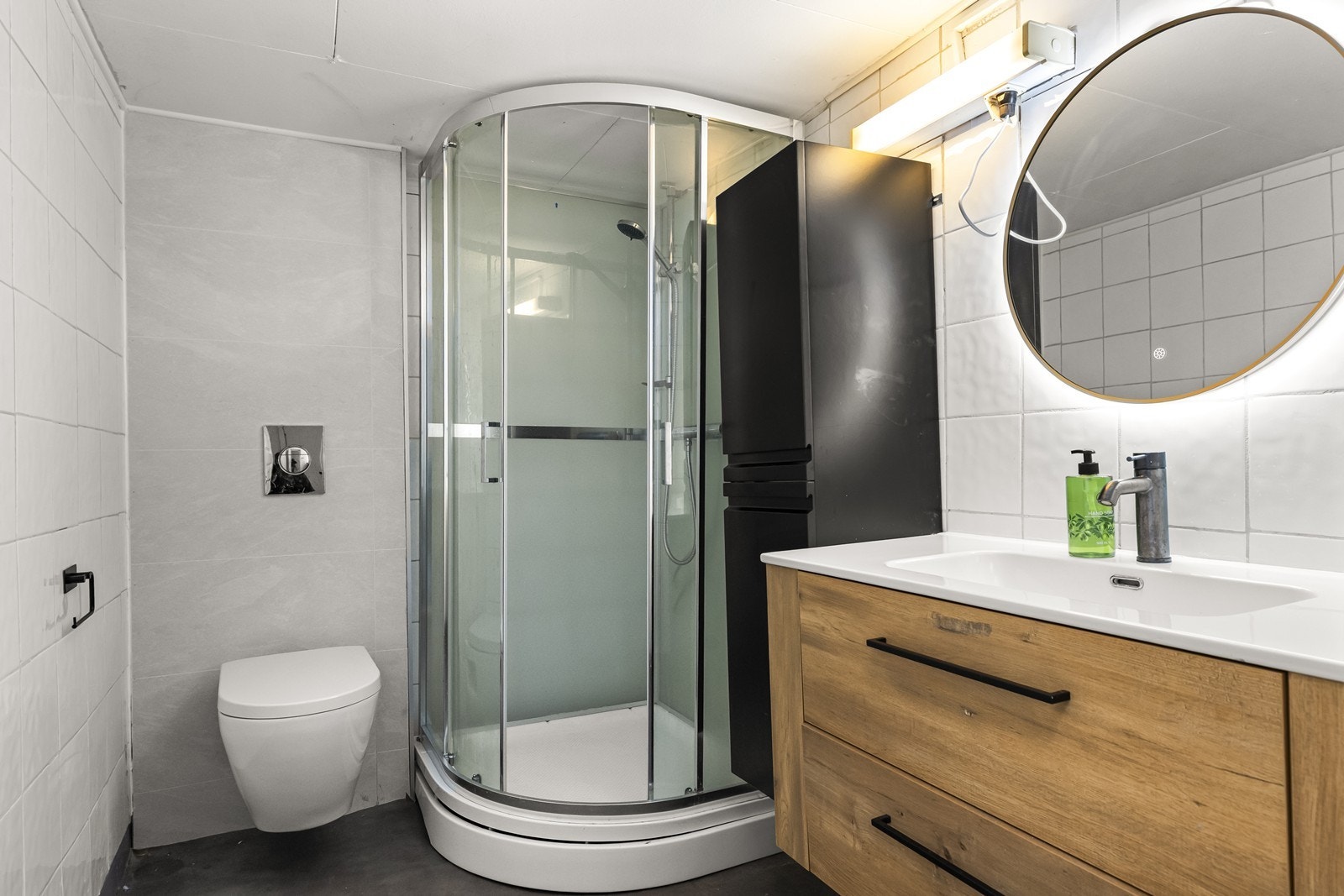 Eldre baderom i kjelleren med vegghengt toalett, dusjkabinett og servantinnredning. Galleribilde