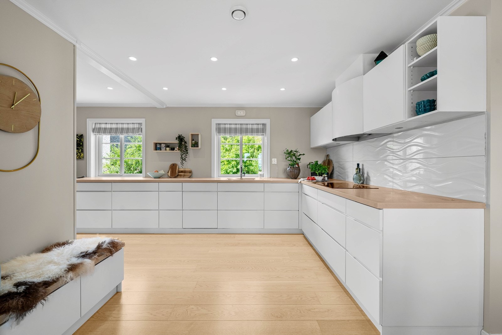 Kjøkkeninnredning med glatte fronter og laminert benkeplate med fliser på deler av vegg over benkeplaten. Det er avtrekk via balansert anlegg. Galleribilde