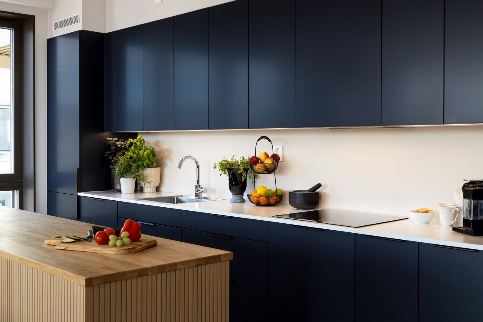 Lekker kjøkkeninnredning med slette lakkerte fronter i mørk blå og lys benkeplate i laminat med nedfelt kum. Kjøkkenet har en stilig kjøkkenøy med finerte fronter og heltre benkeplate Galleribilde